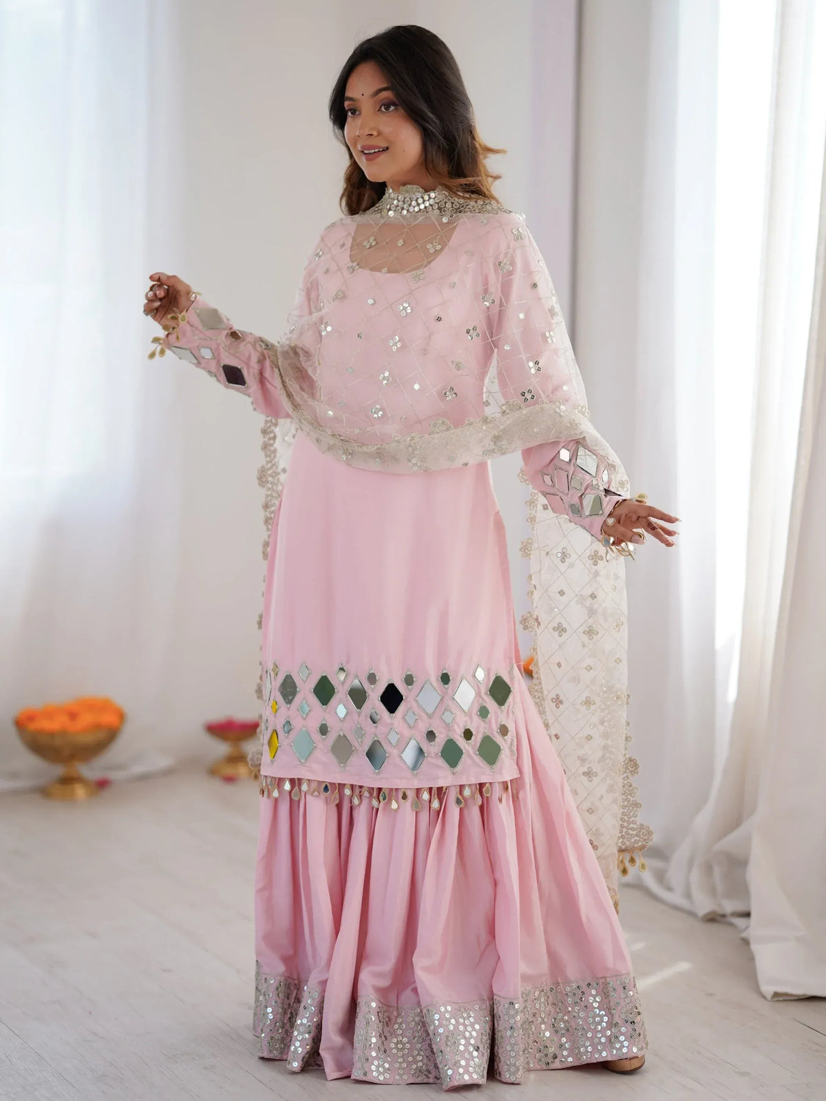 Woman wearing a light pink designer salwar kameez with mirror work and a matching dupatta