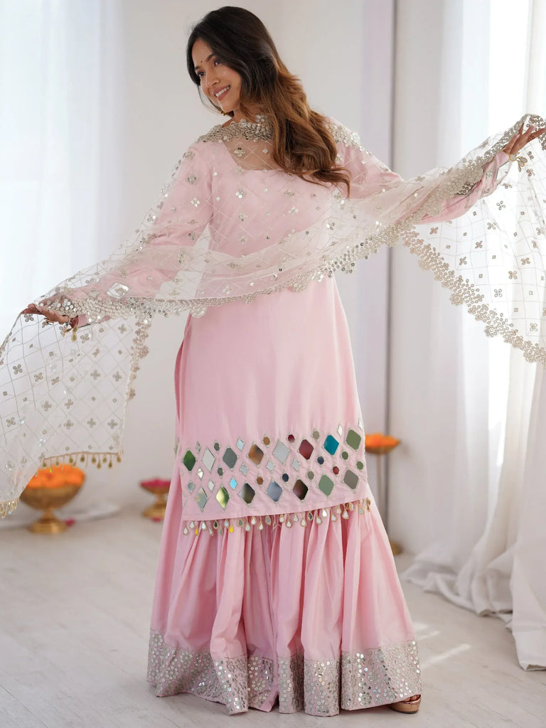 Woman wearing a light pink mirror-work salwar kameez with a matching embellished dupatta