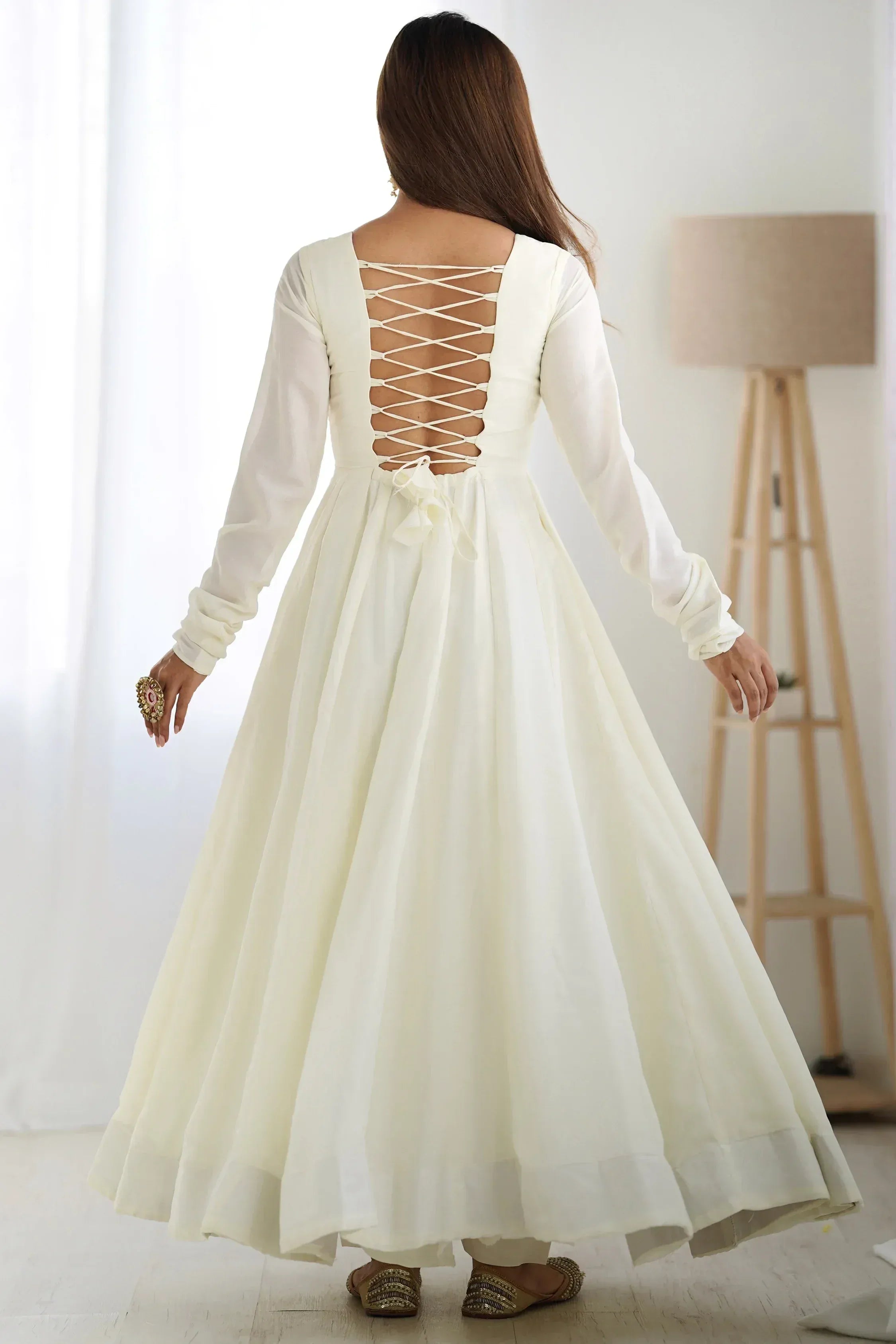 Woman in cream ethnic gown with lace-up back design and long sleeves, indoor setting