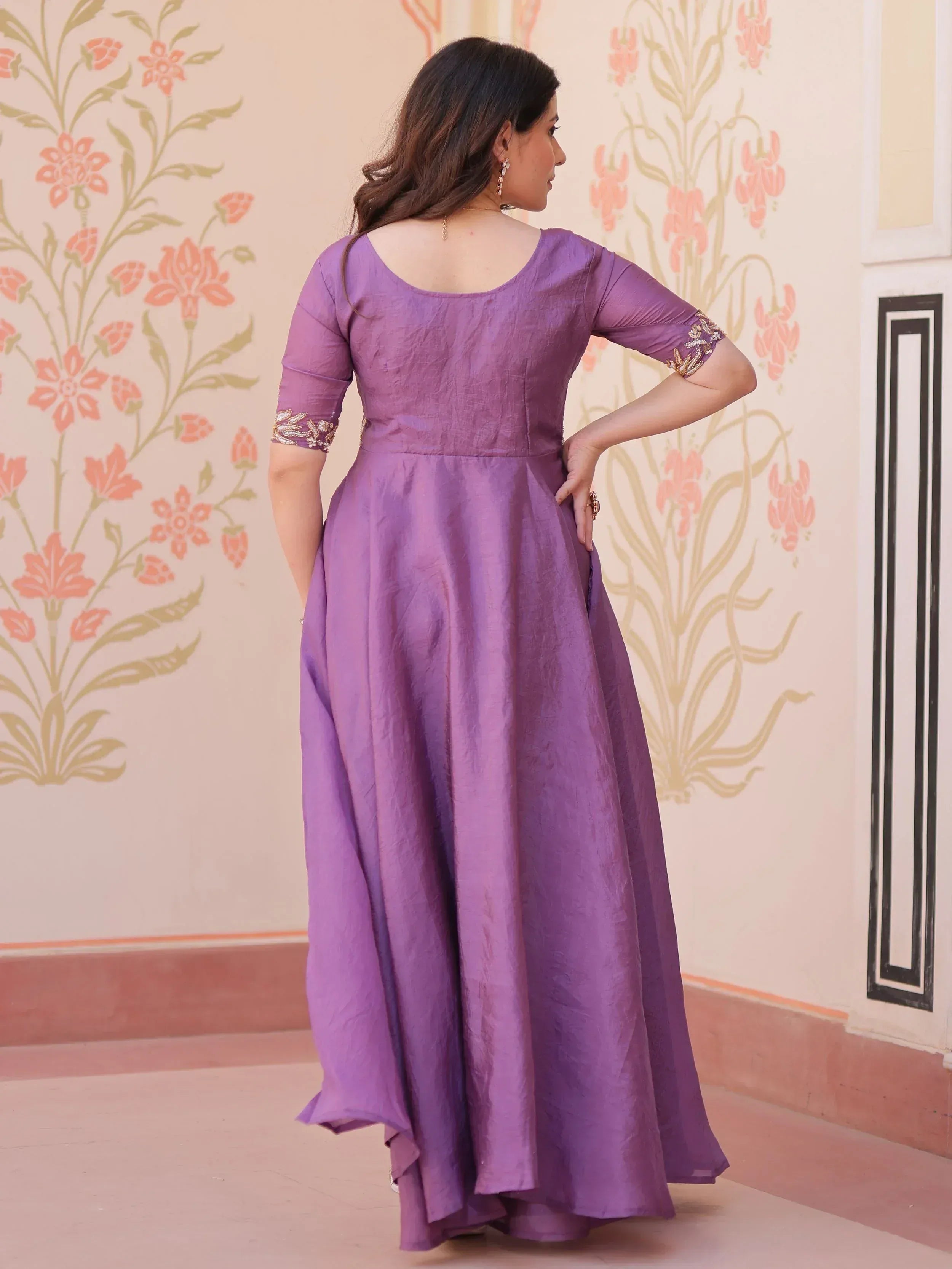 Purple ethnic gown with embroidered sleeves, back view, floral wall backdrop