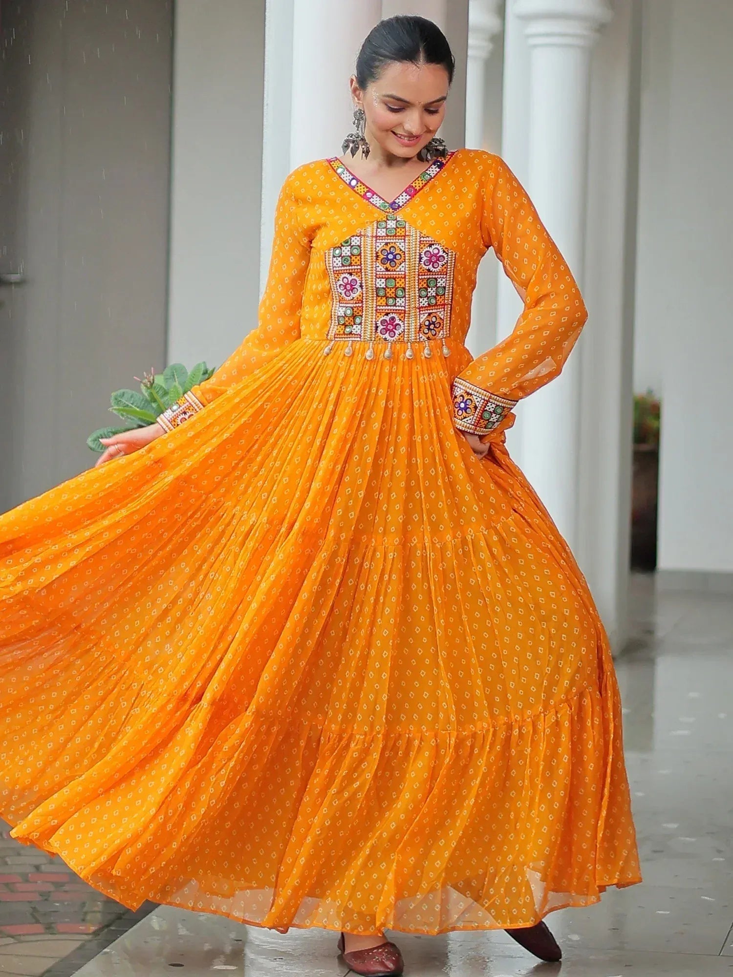Vibrant orange ethnic gown with mirror work, floral embroidery, and pleated skirt for festive occasions