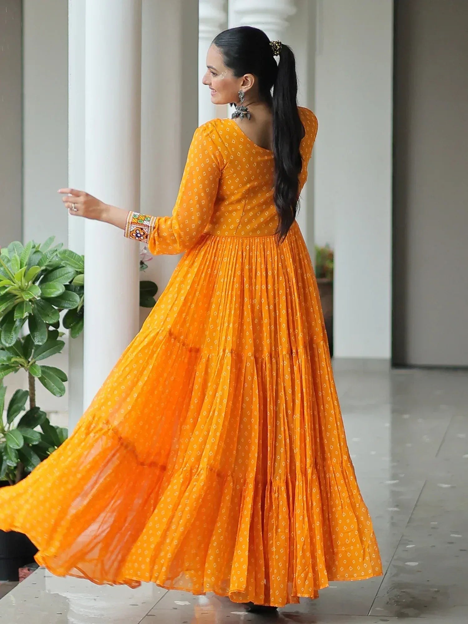 Woman in vibrant orange ethnic gown with pleated skirt and embroidered sleeves, perfect for Indian occasions