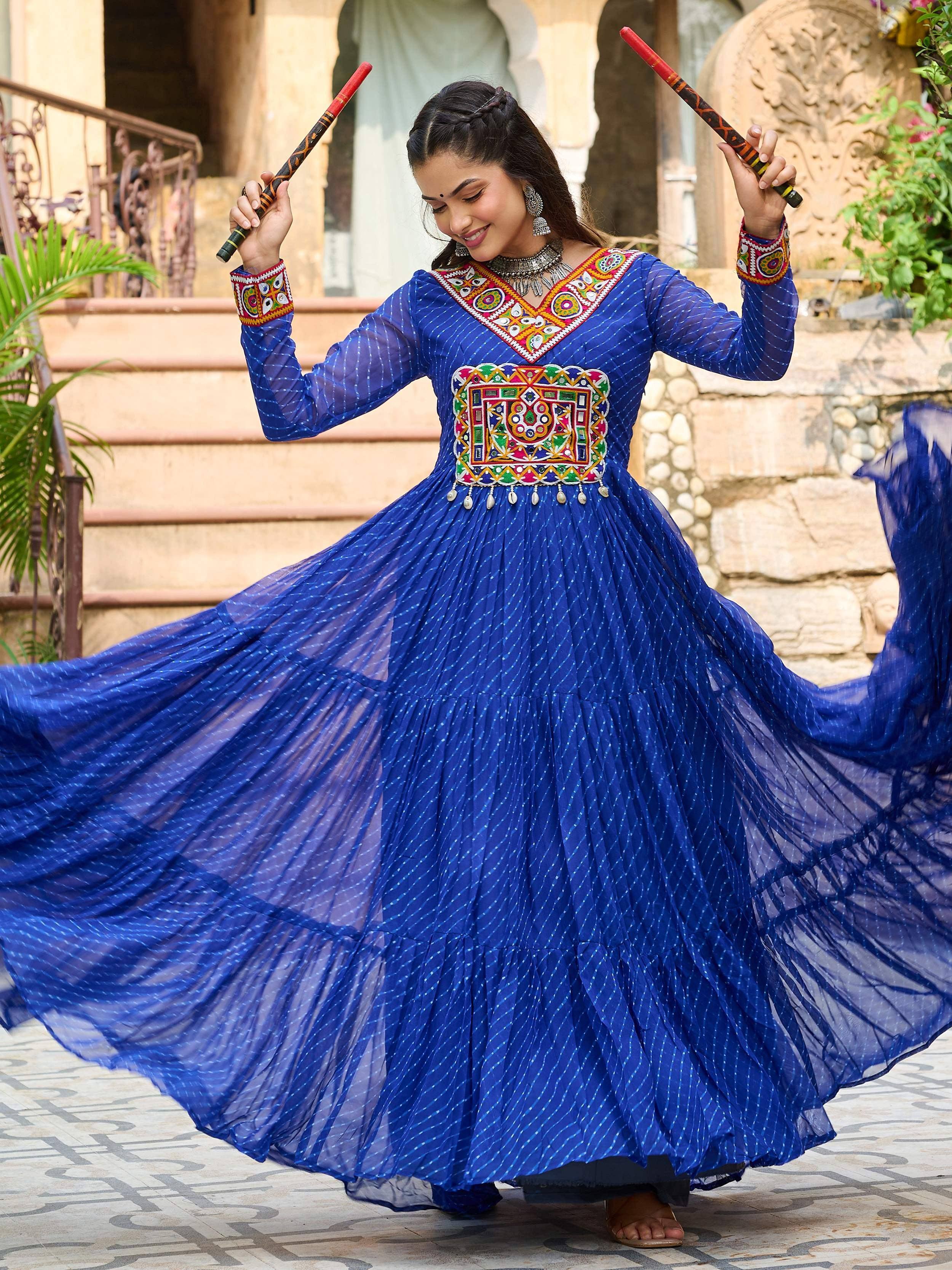 Woman dancing in vibrant blue ethnic gown with mirror work, holding dandiya sticks, perfect for festive occasions.