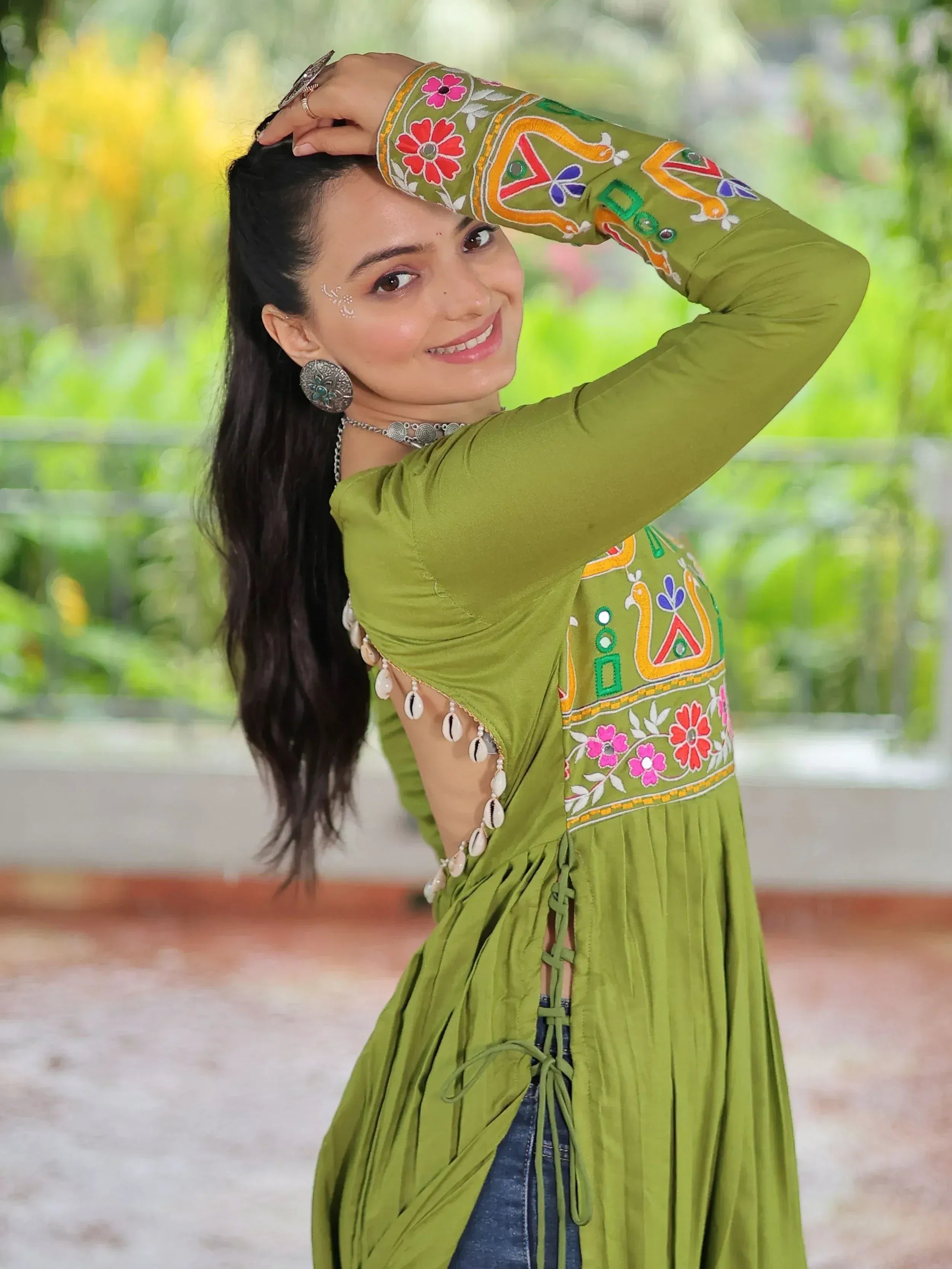 Woman in olive green embroidered ethnic gown with floral and mirror work, paired with denim, perfect for festive occasions.