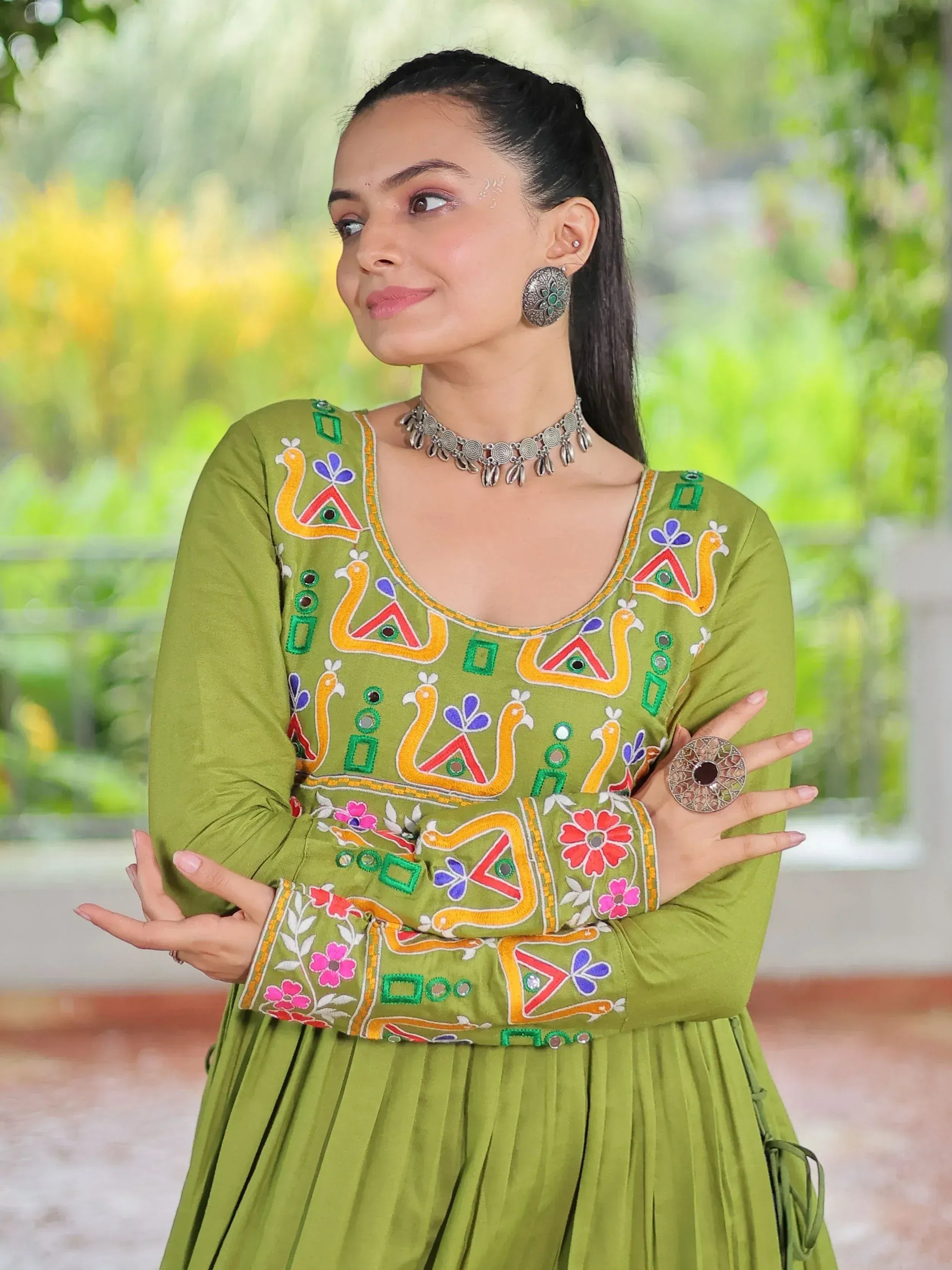 Woman in olive green ethnic gown with colorful embroidery, peacock motifs, and silver jewelry