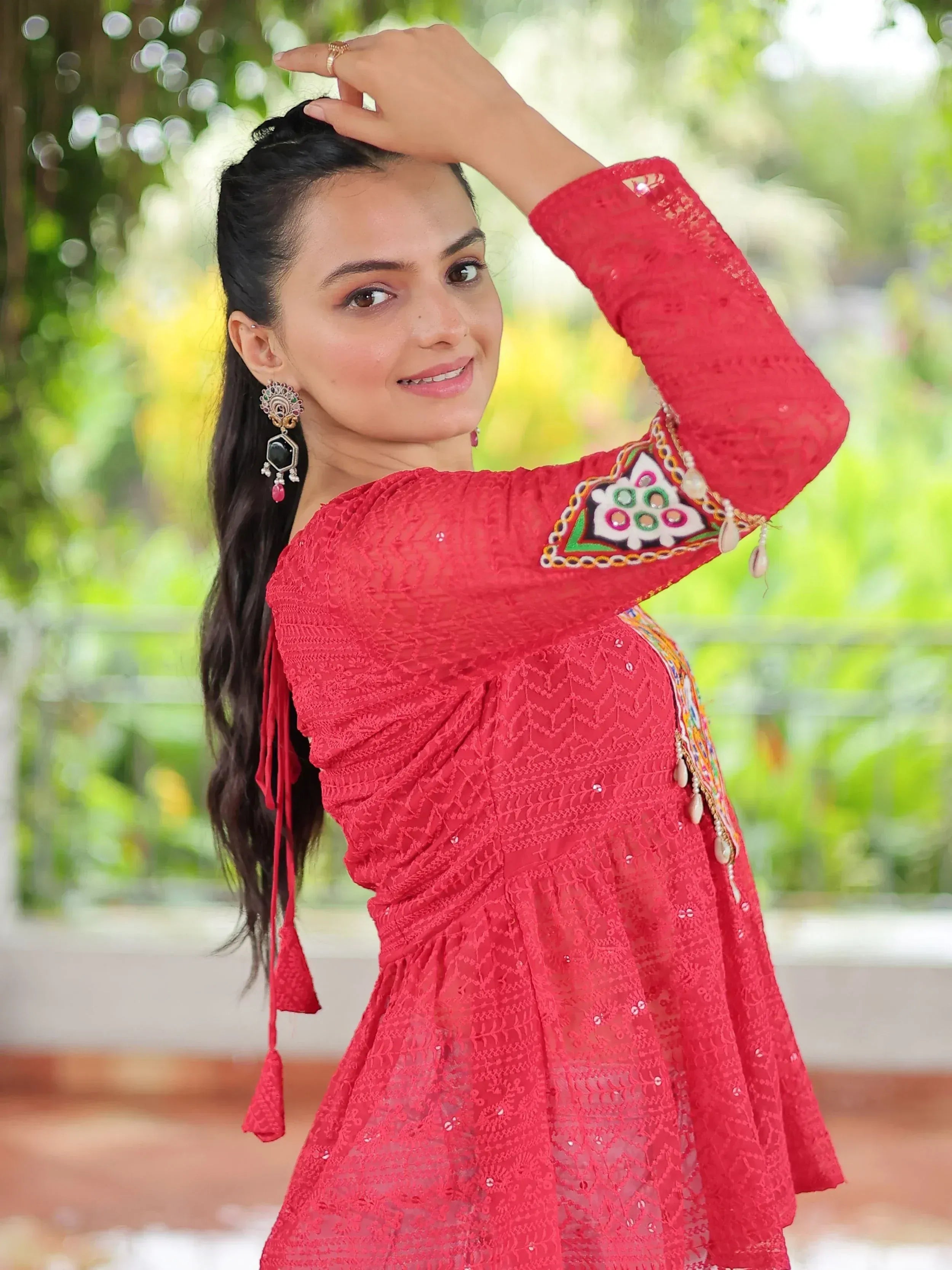 Woman in vibrant red ethnic gown with intricate embroidery and tassels, perfect for festive occasions.