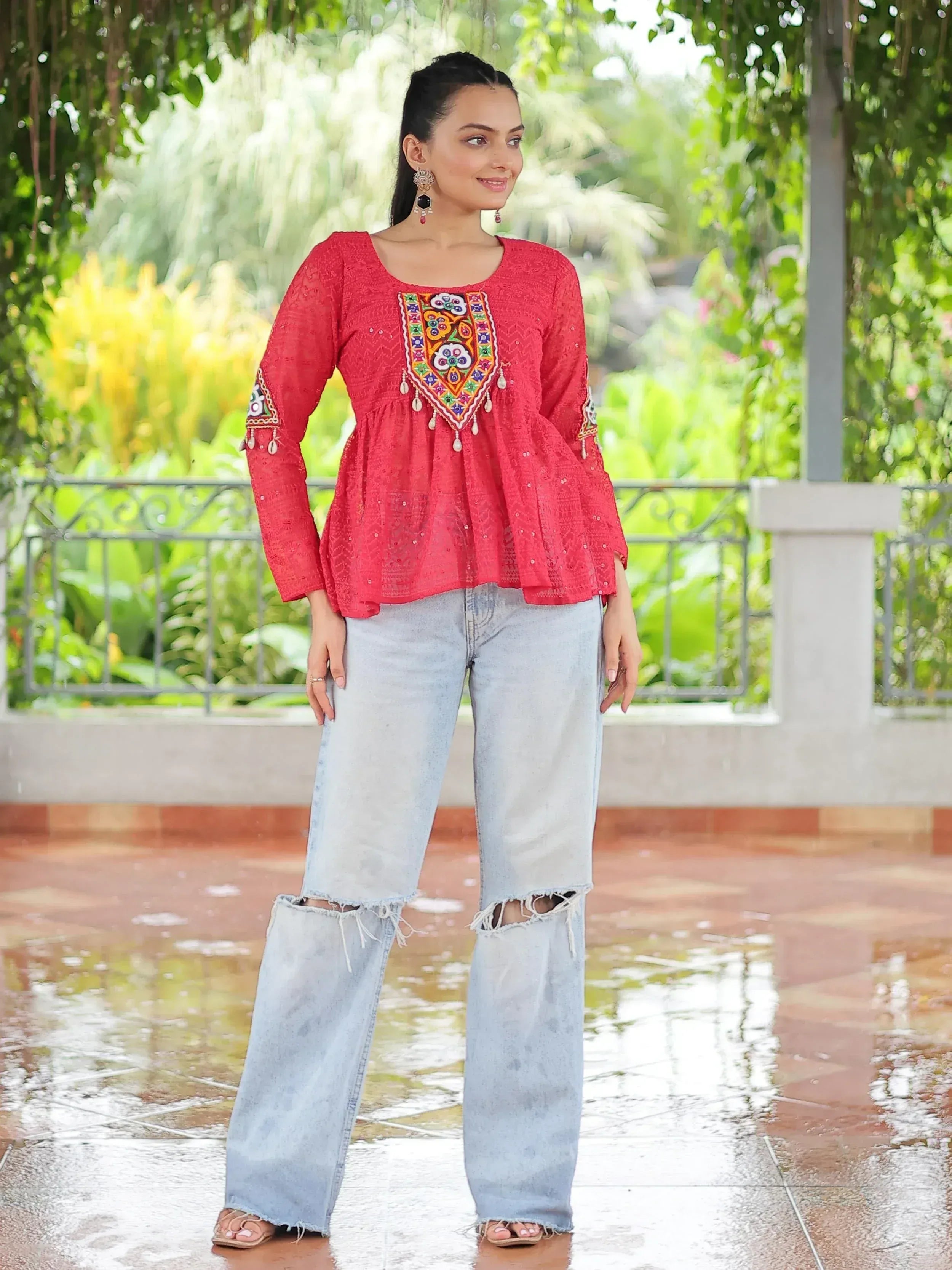 Red embroidered ethnic top with mirror work, paired with ripped wide-leg jeans for casual fusion style