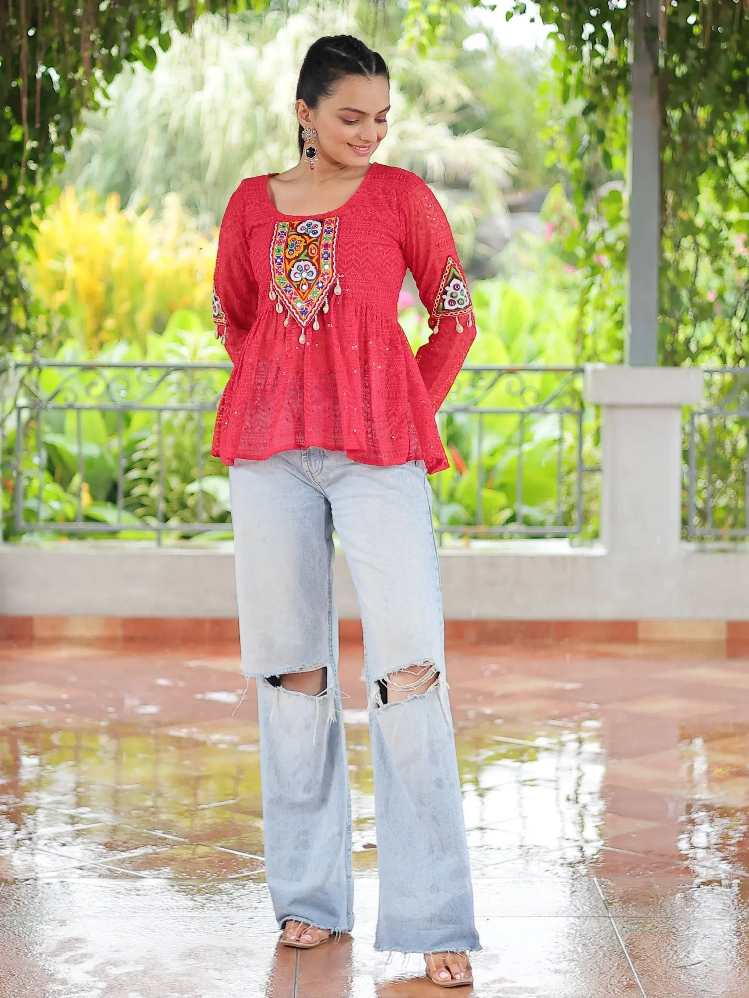 Red embroidered ethnic top with mirror work, paired with ripped jeans, perfect for casual Indian wear.