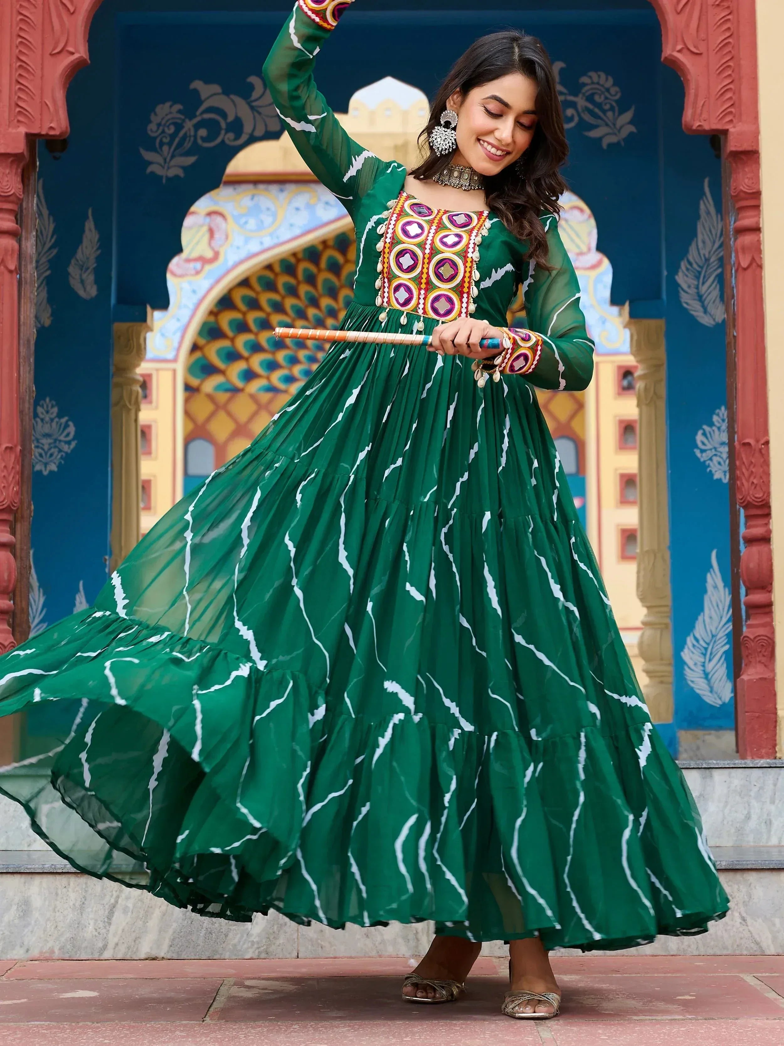 Woman in green ethnic gown with mirror work, dancing at colorful Indian palace entrance