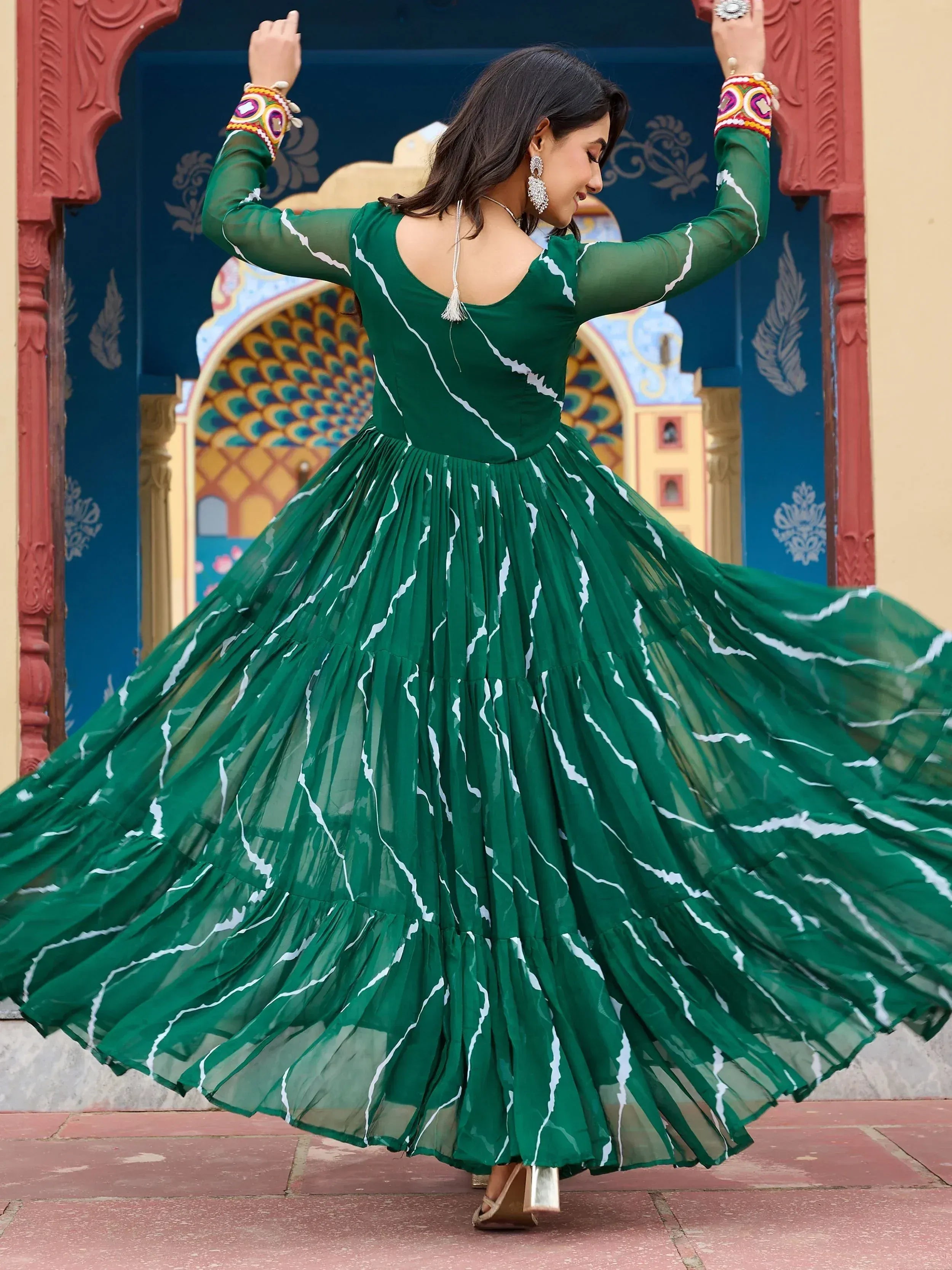 Woman twirling in green ethnic gown with white print, long sleeves, and pleated skirt, perfect for Indian occasions.