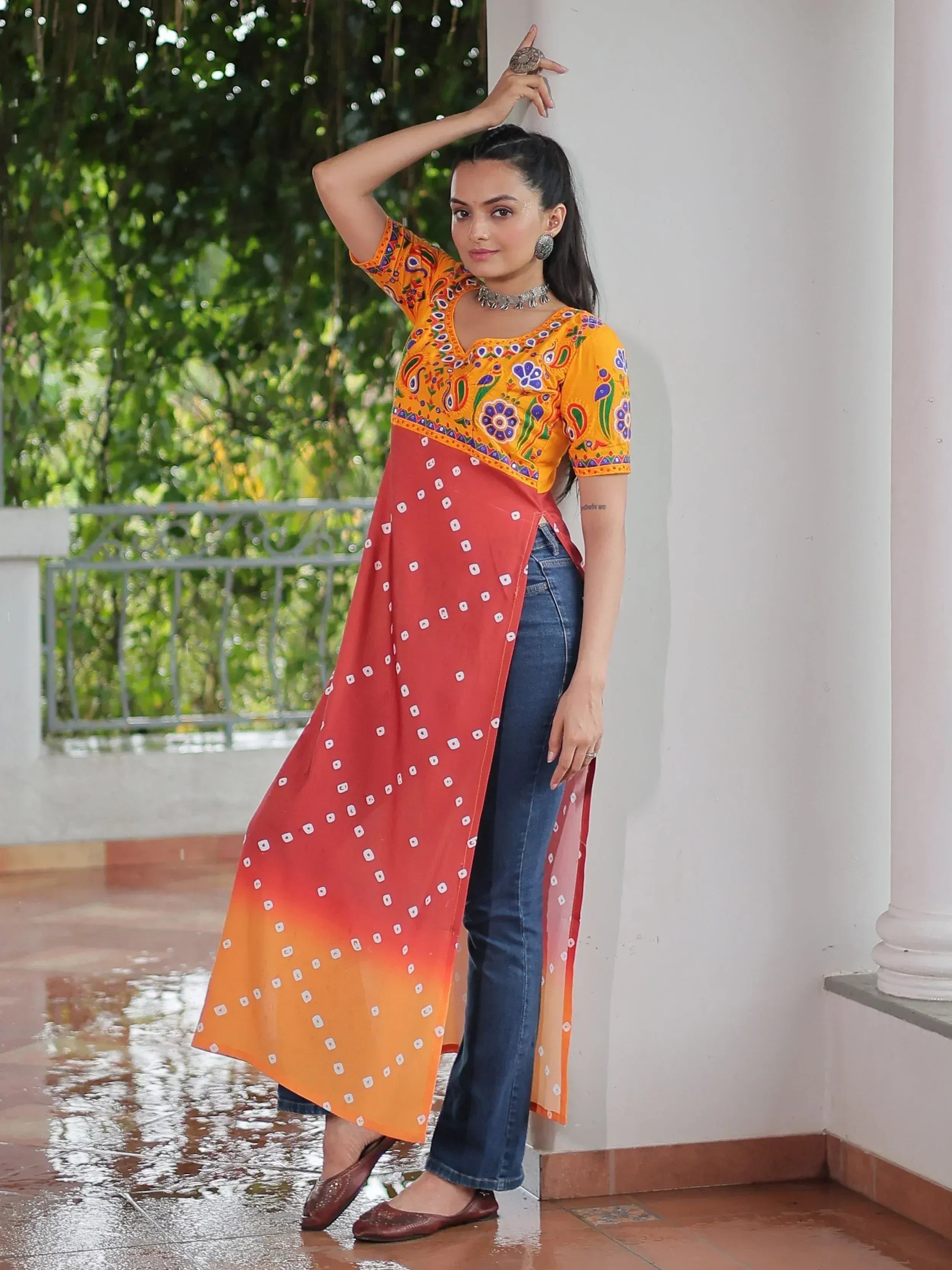 Woman in vibrant yellow and red ethnic kurti with floral embroidery, paired with jeans, perfect for casual Indian wear.