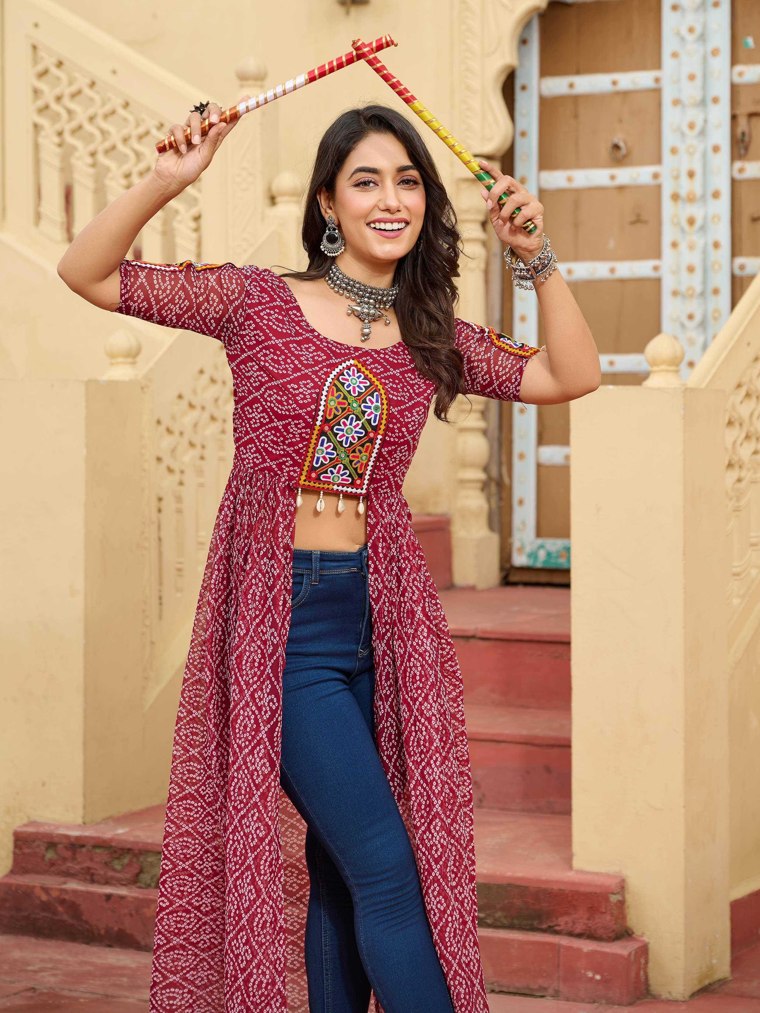 Woman in red printed ethnic kurti with mirror work, paired with jeans, holding colorful sticks, traditional Indian attire