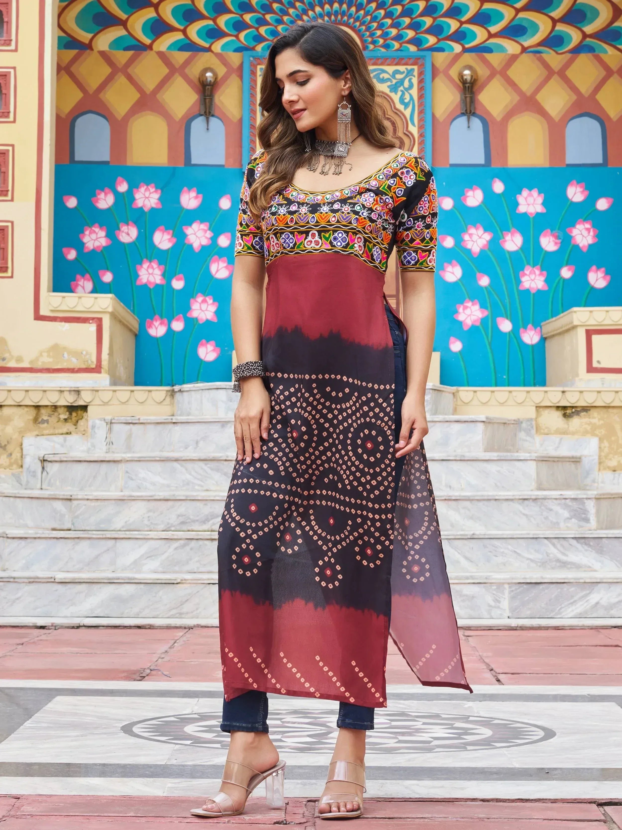Woman in embroidered ethnic kurti with tie-dye print, paired with jeans, against colorful Indian mural backdrop