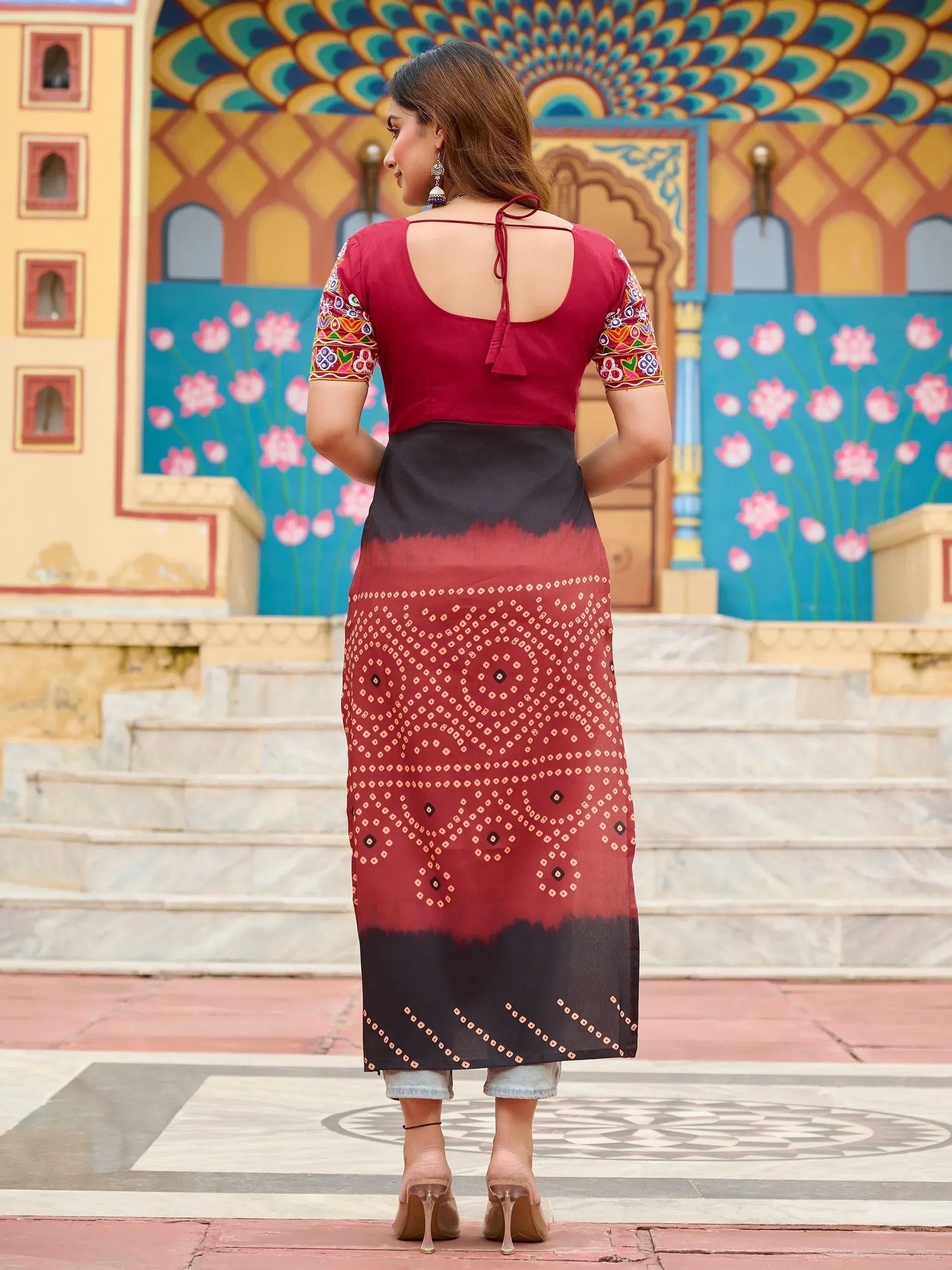 Maroon and black ethnic kurta with embroidered sleeves and back tie, paired with jeans, against colorful Indian architecture