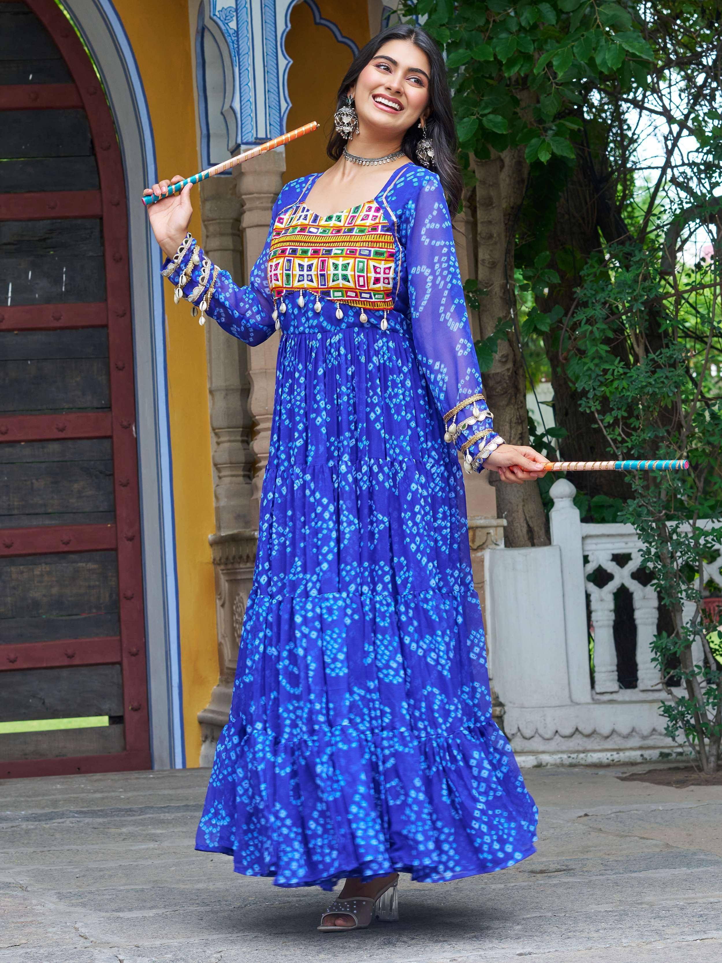 Woman in vibrant blue ethnic gown with mirror work, holding dandiya sticks, perfect for festive occasions.