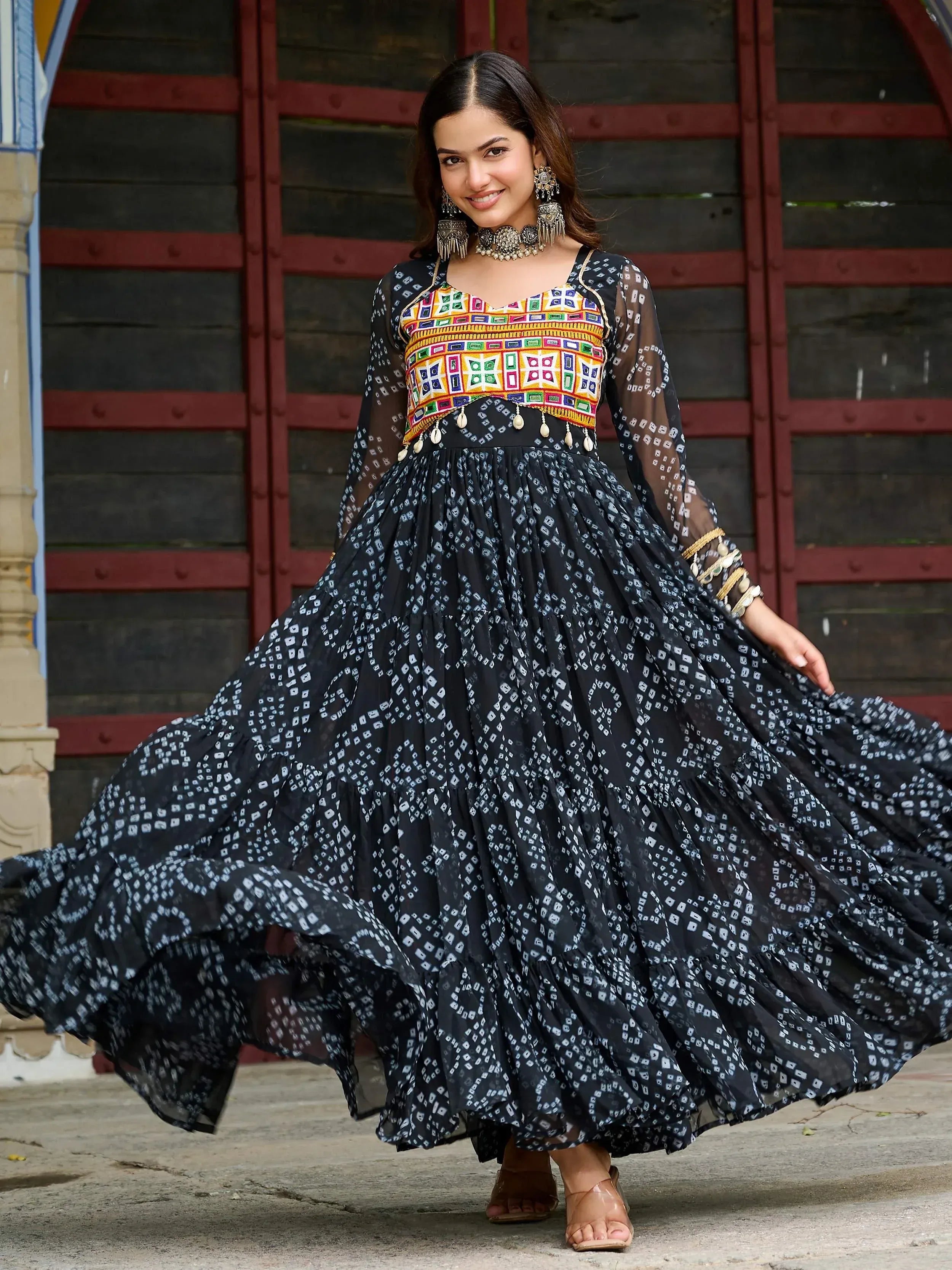Woman in black printed ethnic gown with colorful embroidered bodice and sheer sleeves, perfect for festive occasions.
