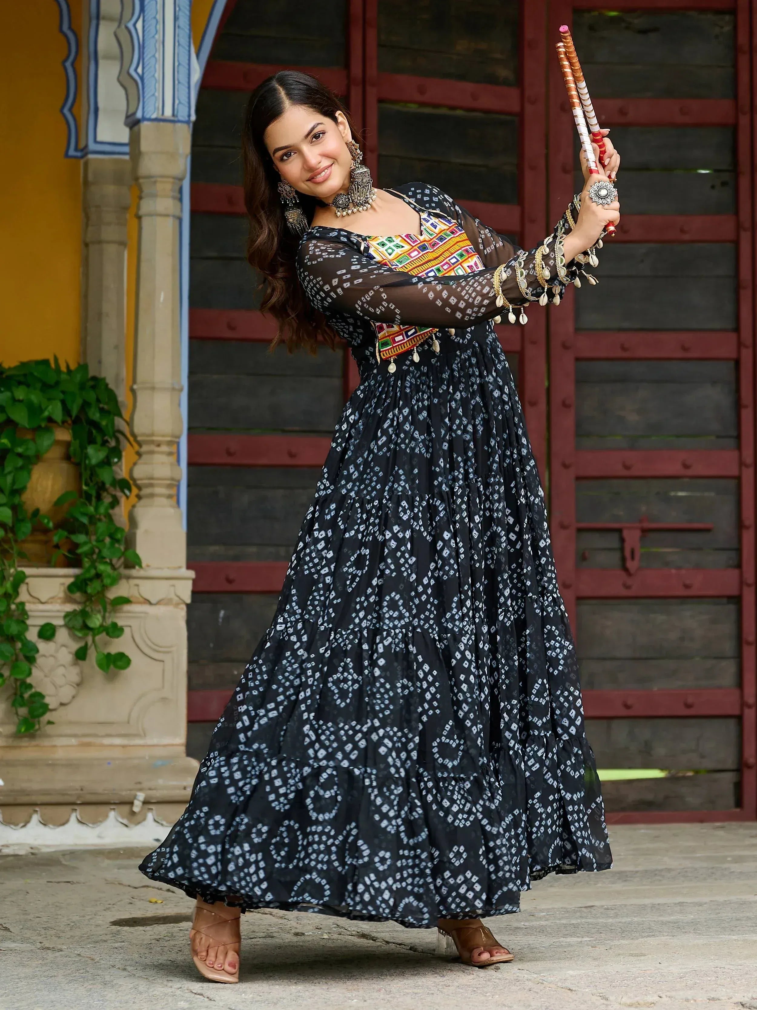 Woman in black and white printed ethnic gown with colorful embroidery, holding dandiya sticks, traditional Indian attire