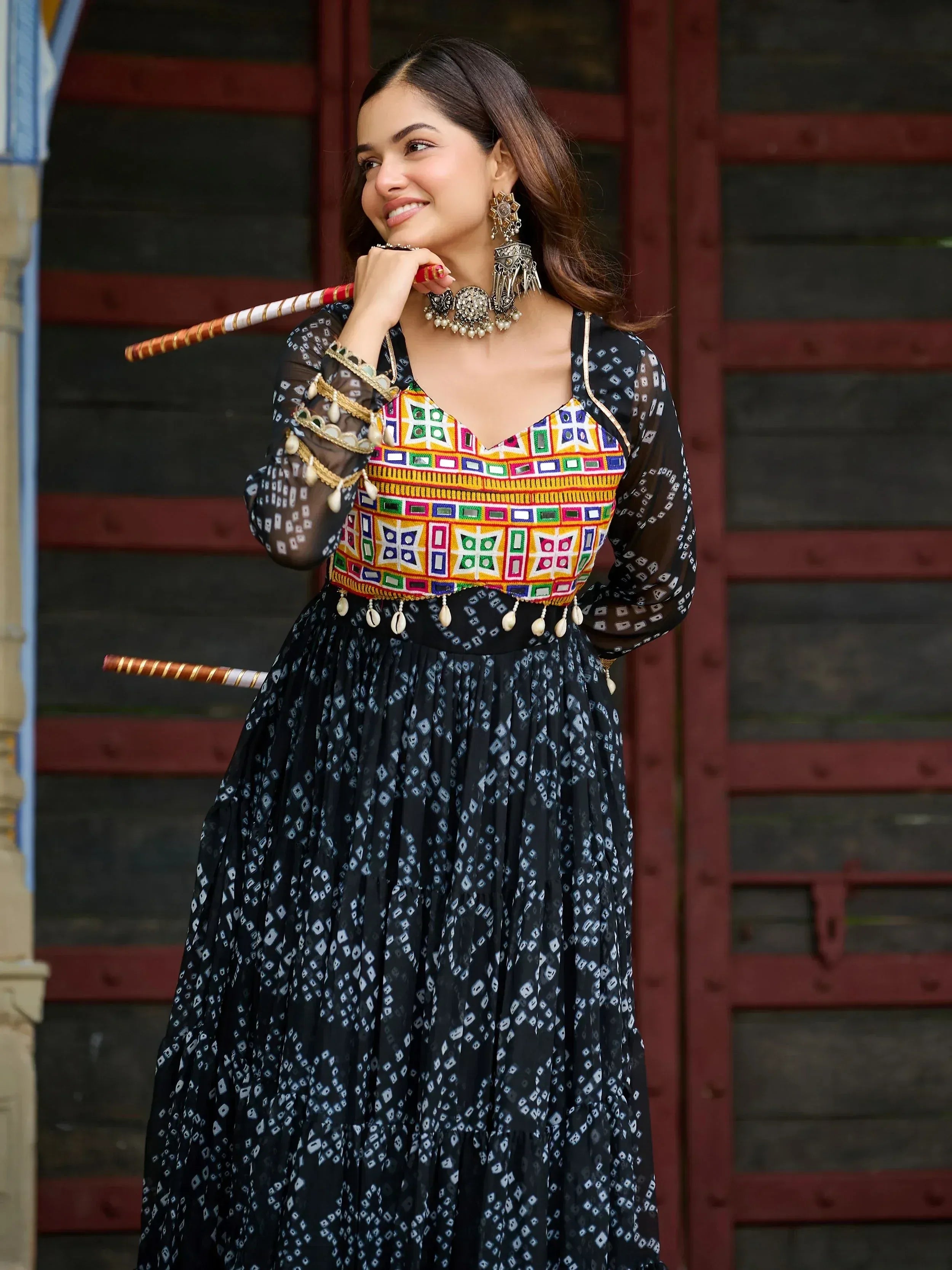 Woman in colorful embroidered ethnic gown with mirror work, holding decorative stick, traditional Indian attire
