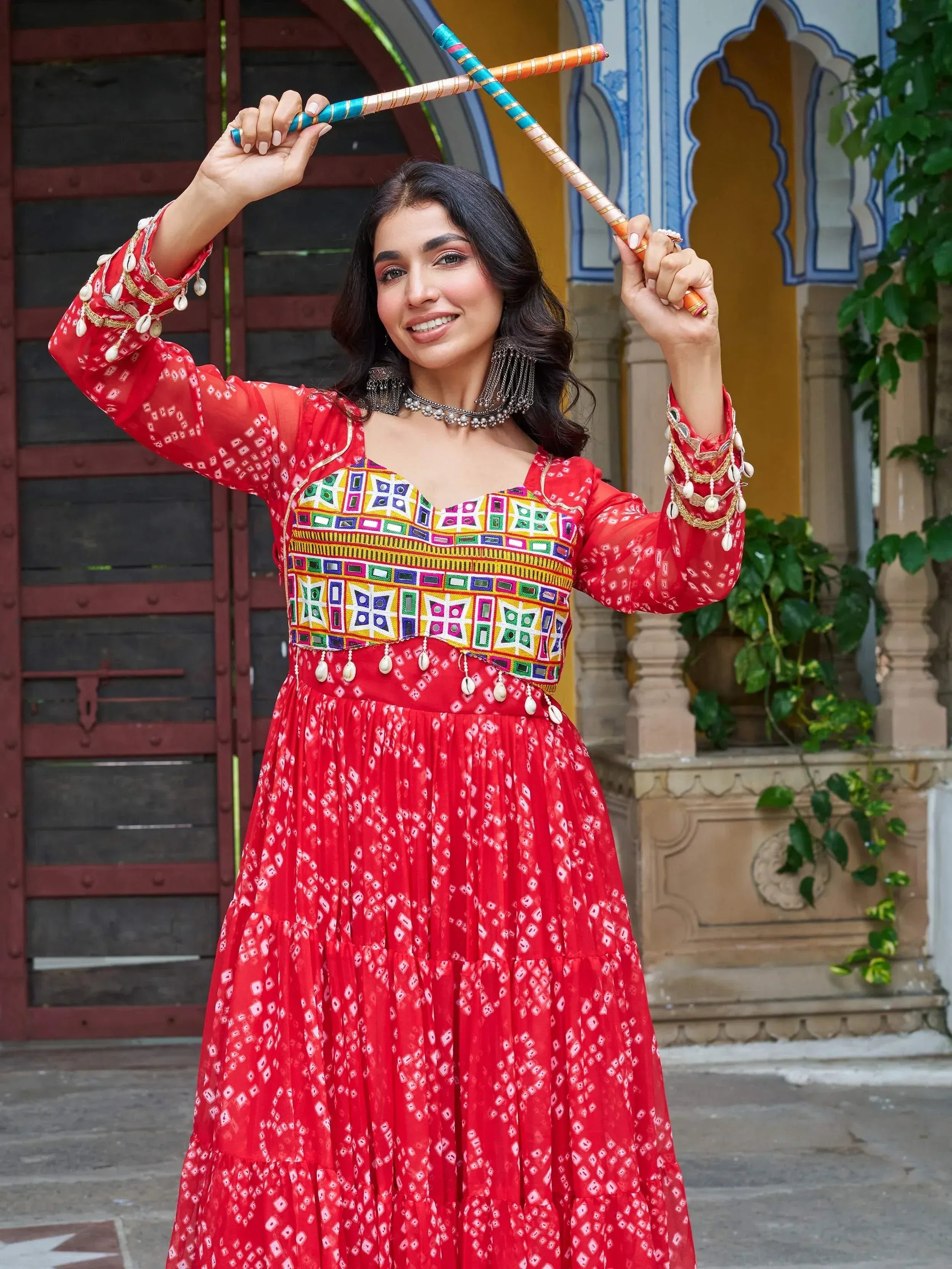 Woman in red ethnic gown with mirror work, holding dandiya sticks, traditional Indian festive wear