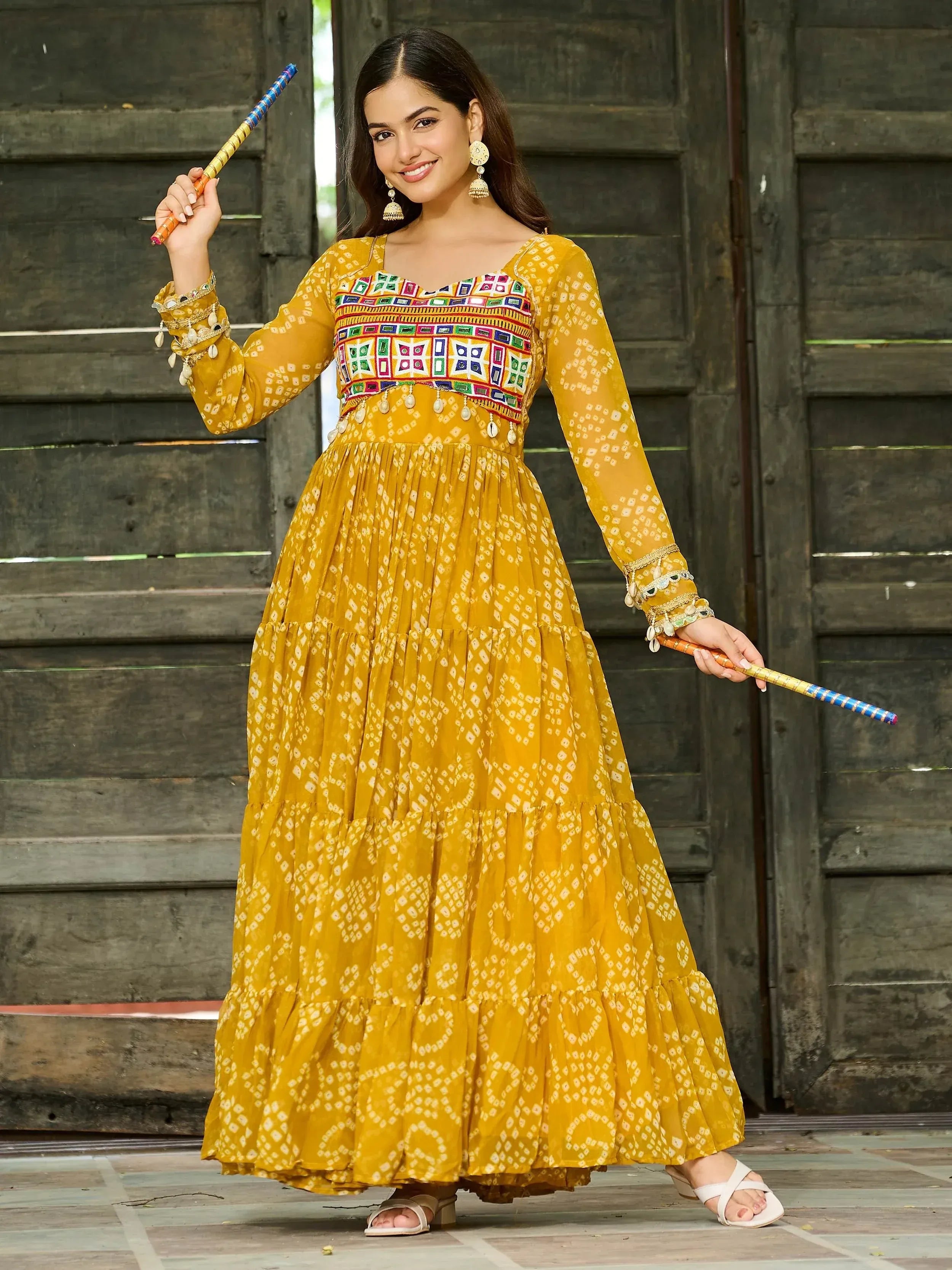 Yellow ethnic gown with mirror work and tiered skirt, paired with traditional accessories