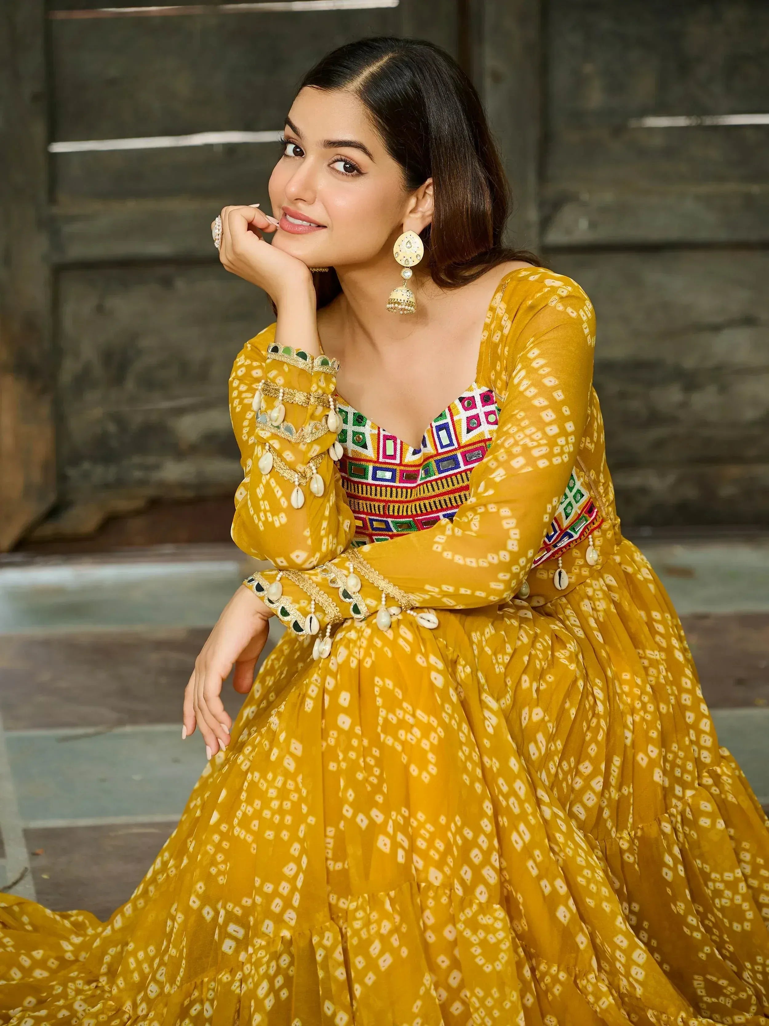 Woman in mustard yellow ethnic gown with mirror work and shell embellishments, perfect for Indian occasions