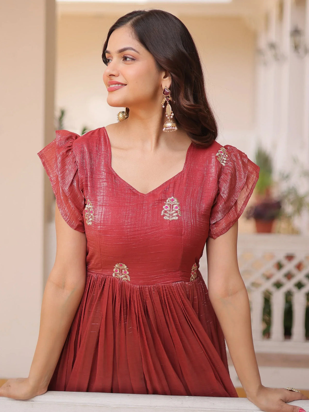 Woman wearing a red ethnic gown with ruffled sleeves and floral embroidery.