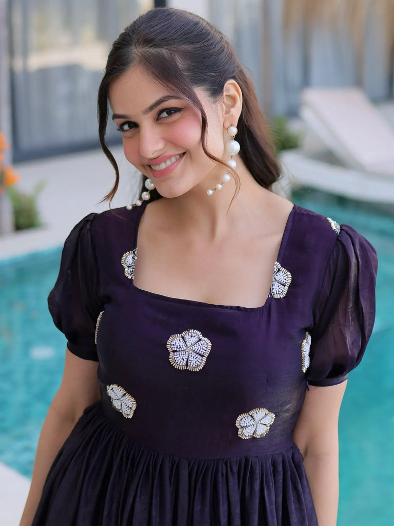 Purple ethnic gown with floral beadwork, puffed sleeves, and pearl earrings, perfect for Indian occasions.