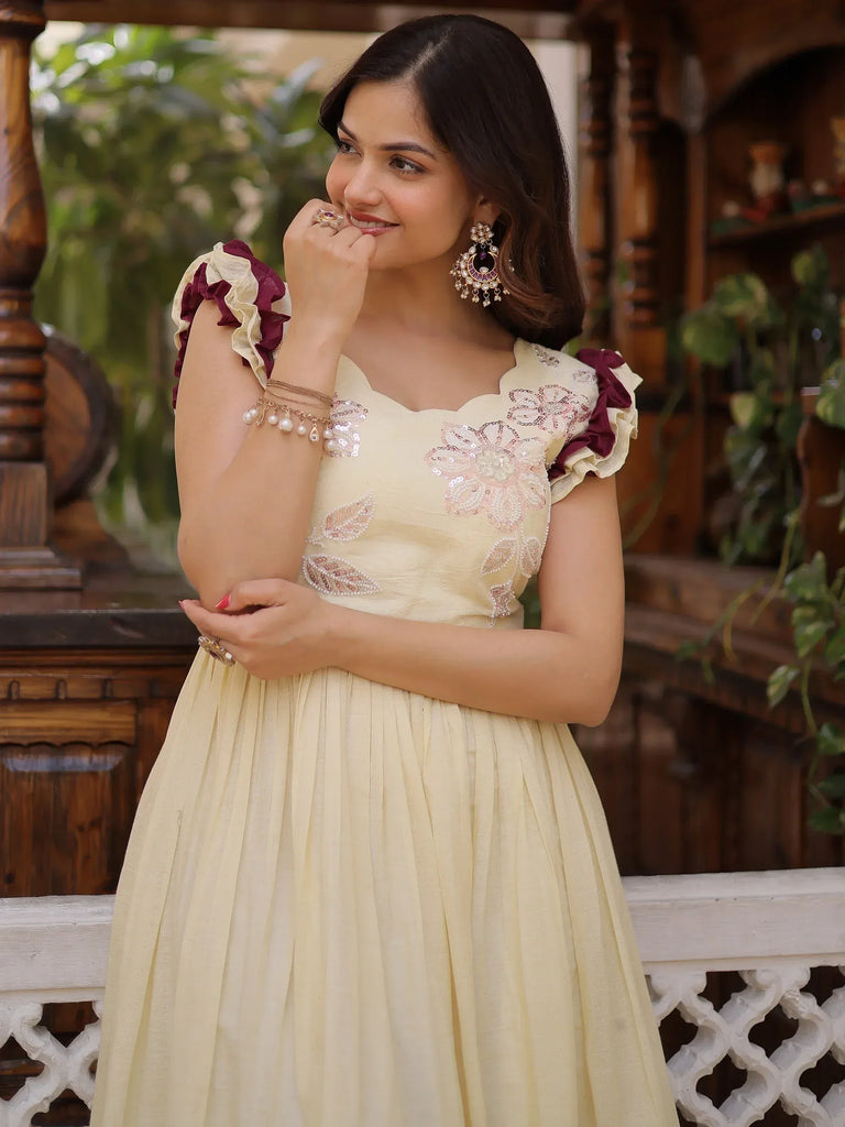 Elegant cream ethnic gown with floral embroidery and ruffled sleeves, perfect for Indian celebrations.