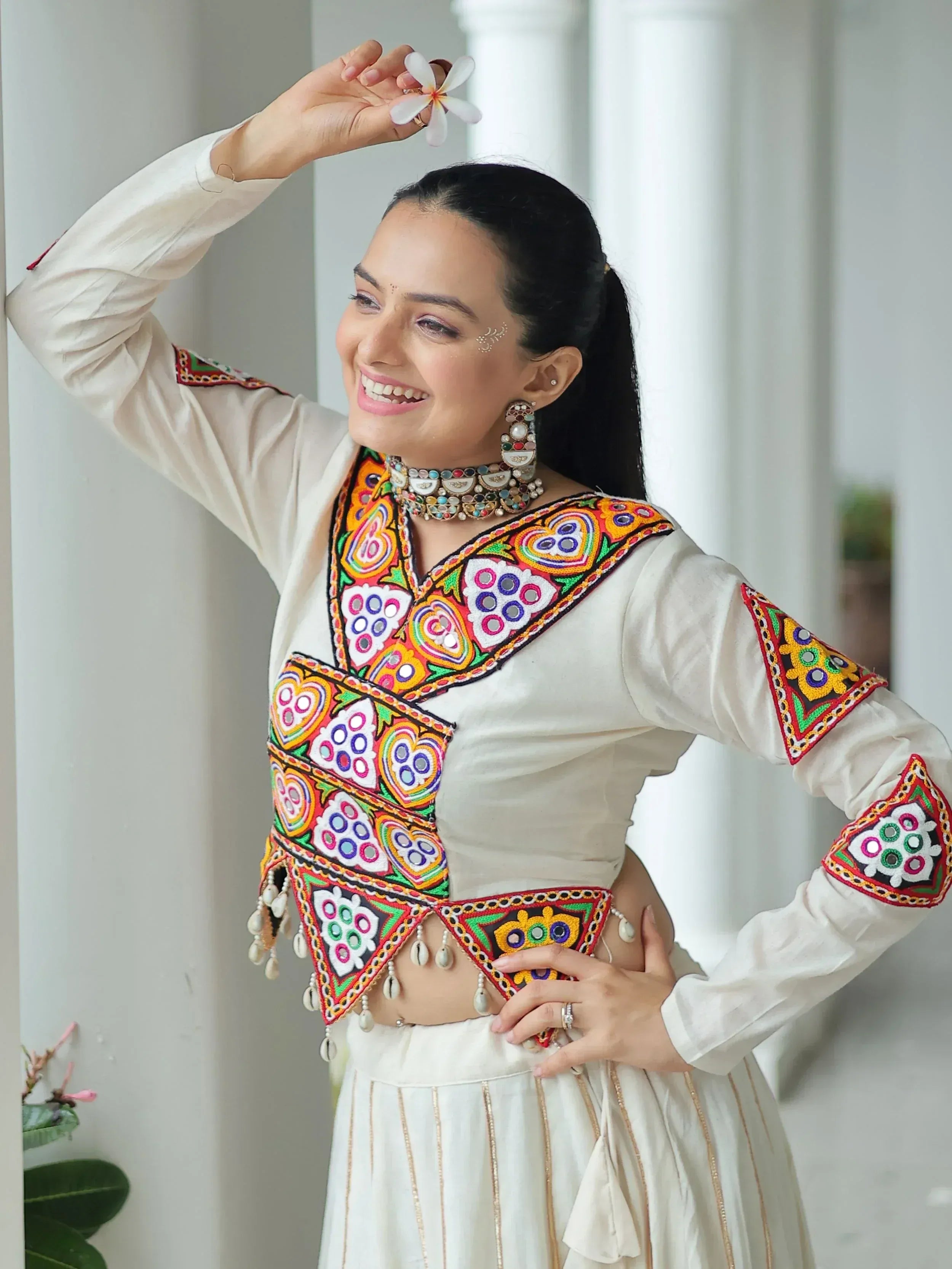Woman in white embroidered ethnic top with colorful mirror work and floral accessories