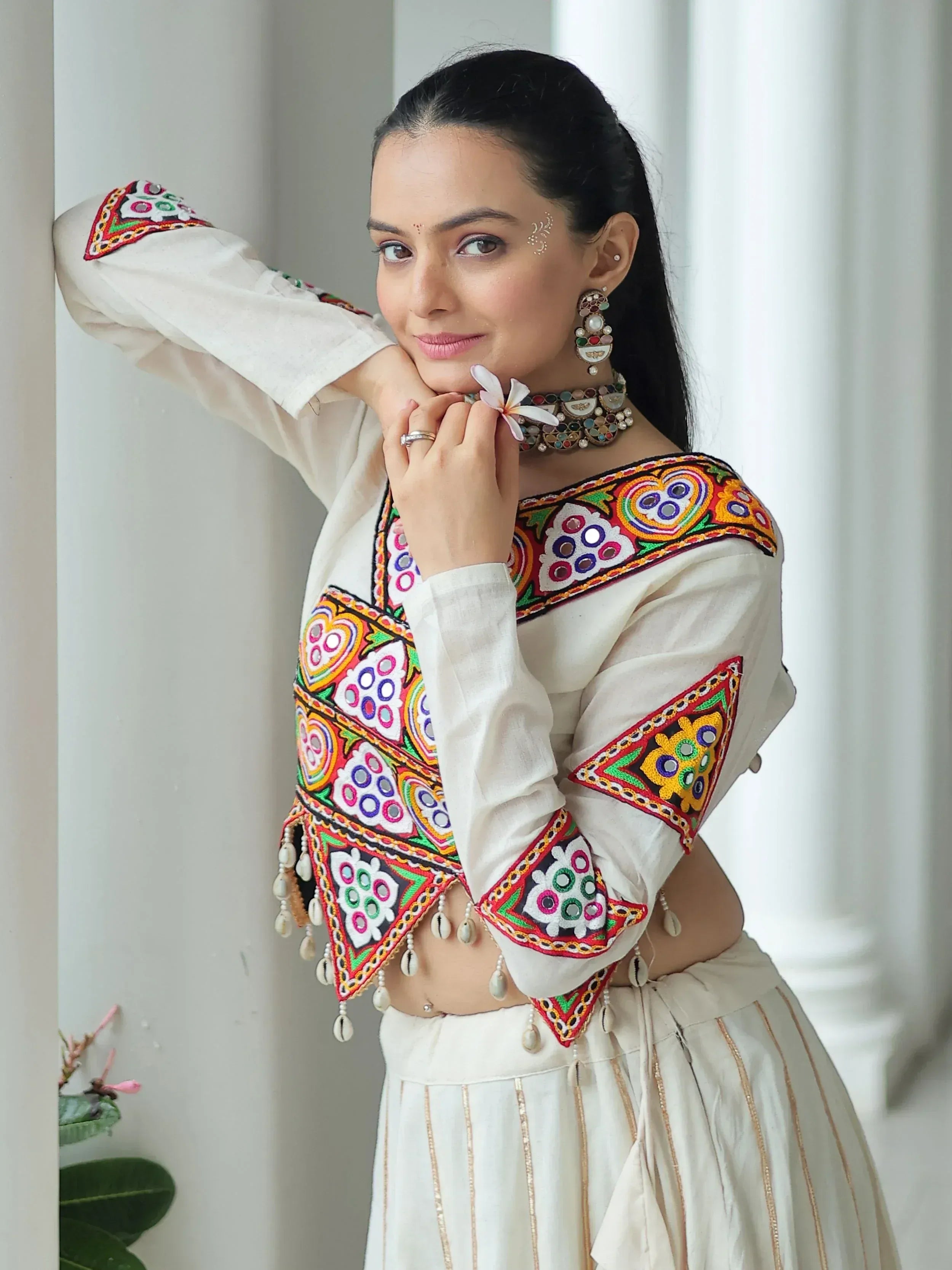 White embroidered ethnic blouse with colorful mirror work and tassels, paired with a matching skirt