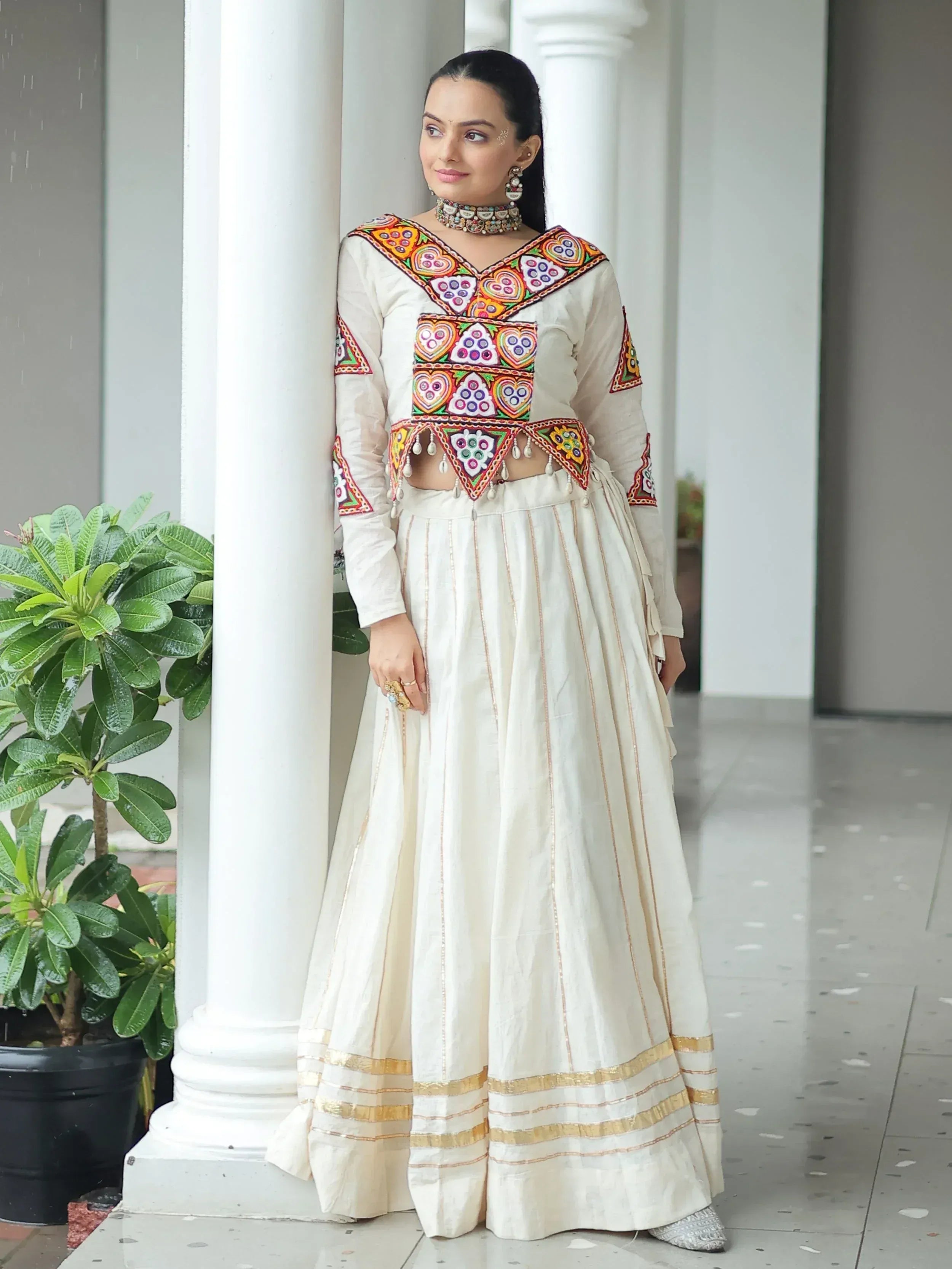 White embroidered lehenga choli with colorful mirror work and gold trim, perfect for Indian ethnic wear.