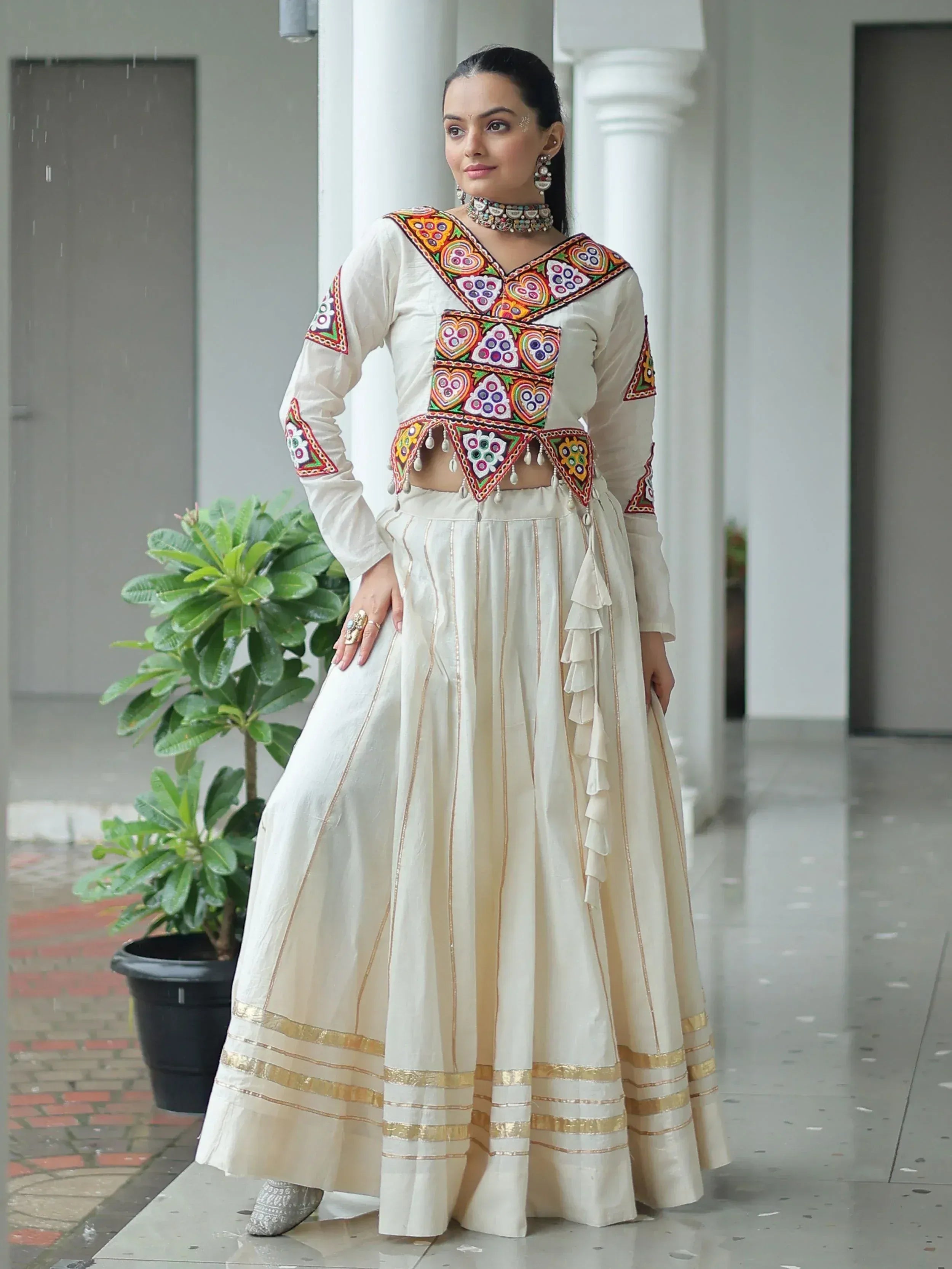 White embroidered ethnic lehenga choli with colorful mirror work and gold trim, perfect for Indian festive wear.