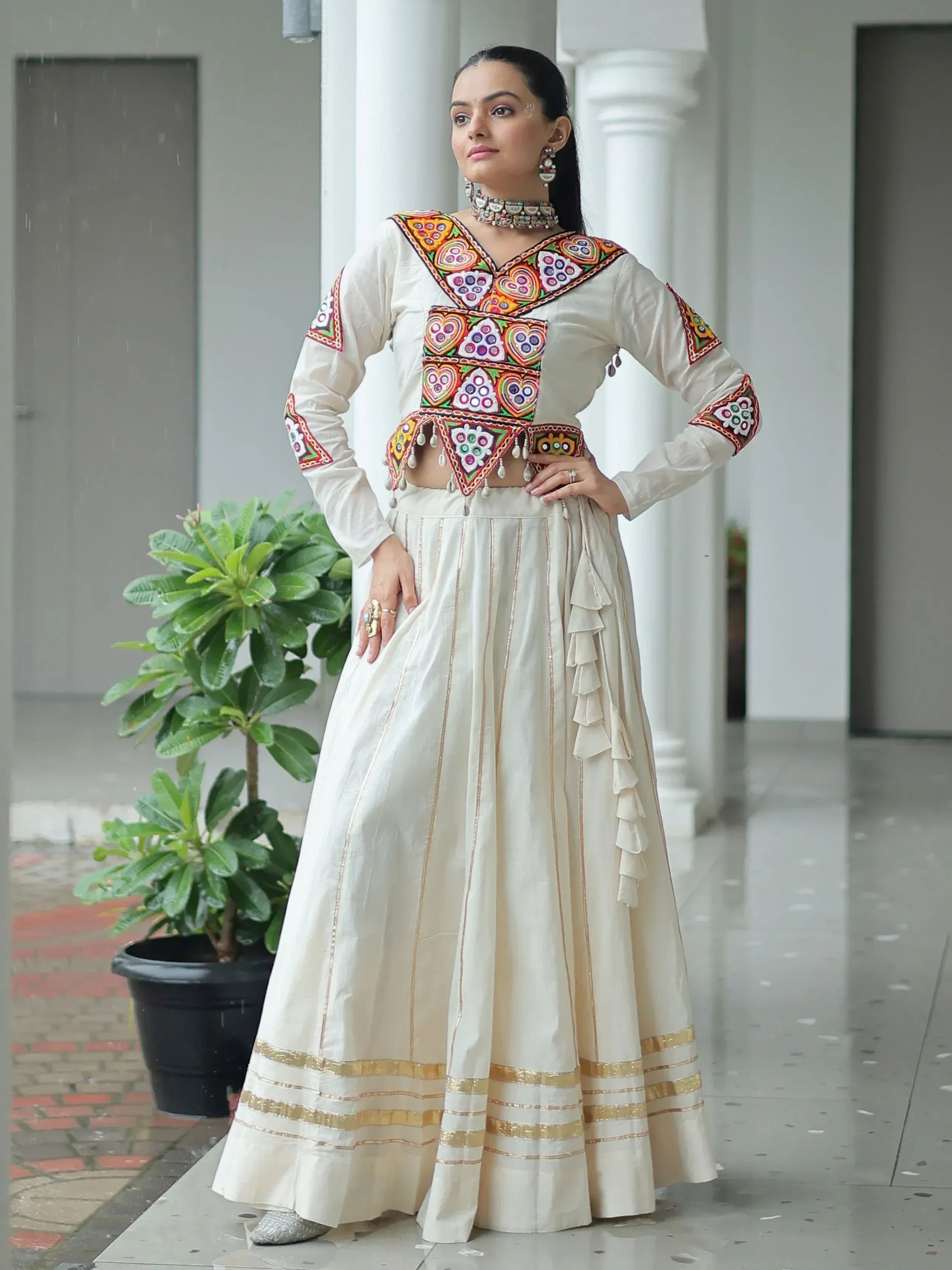 White ethnic lehenga choli with colorful mirror work and gold trim, perfect for Indian weddings or festivals