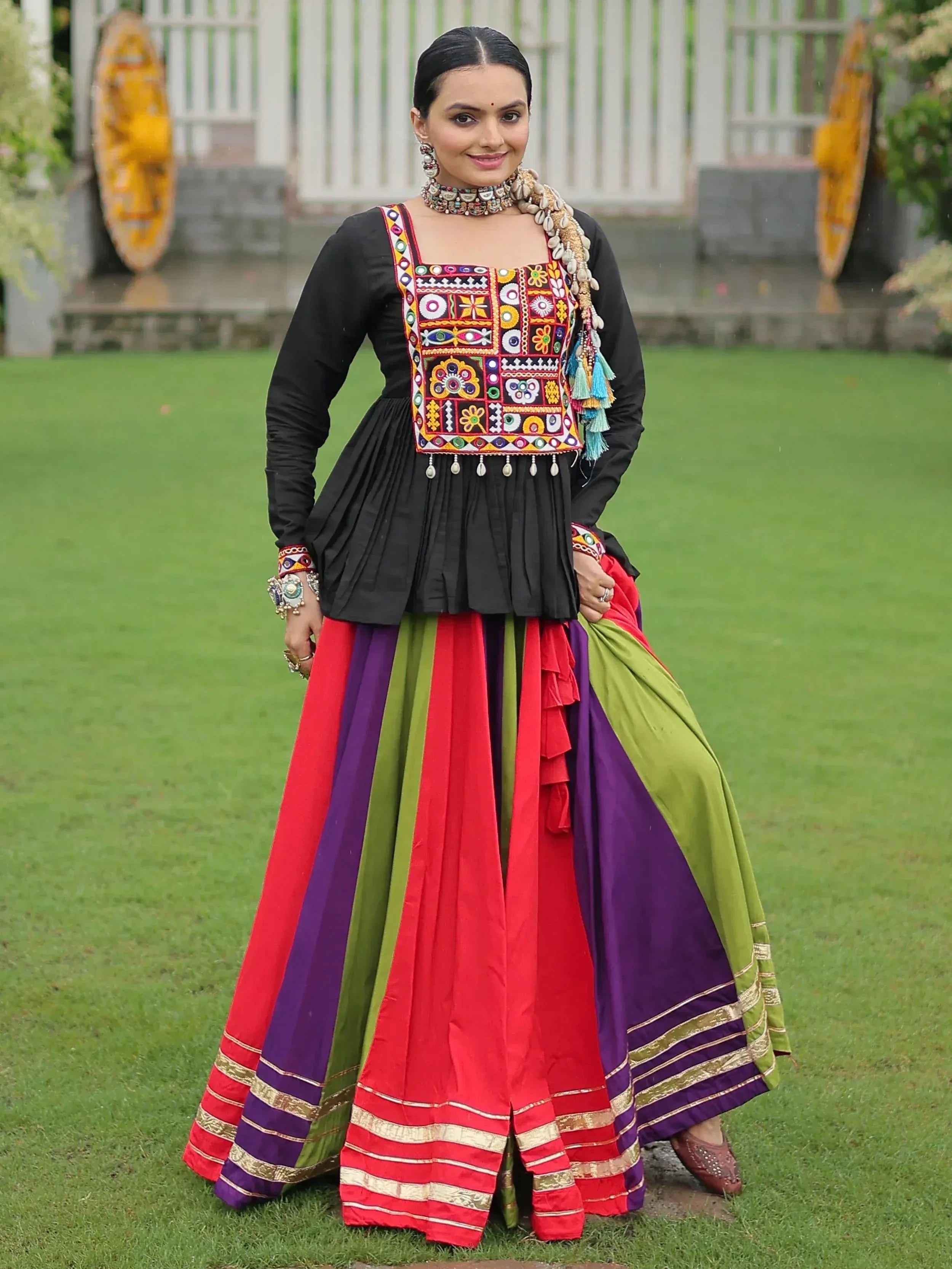 Woman in vibrant Indian ethnic wear with embroidered black top and colorful striped skirt, perfect for festive occasions.