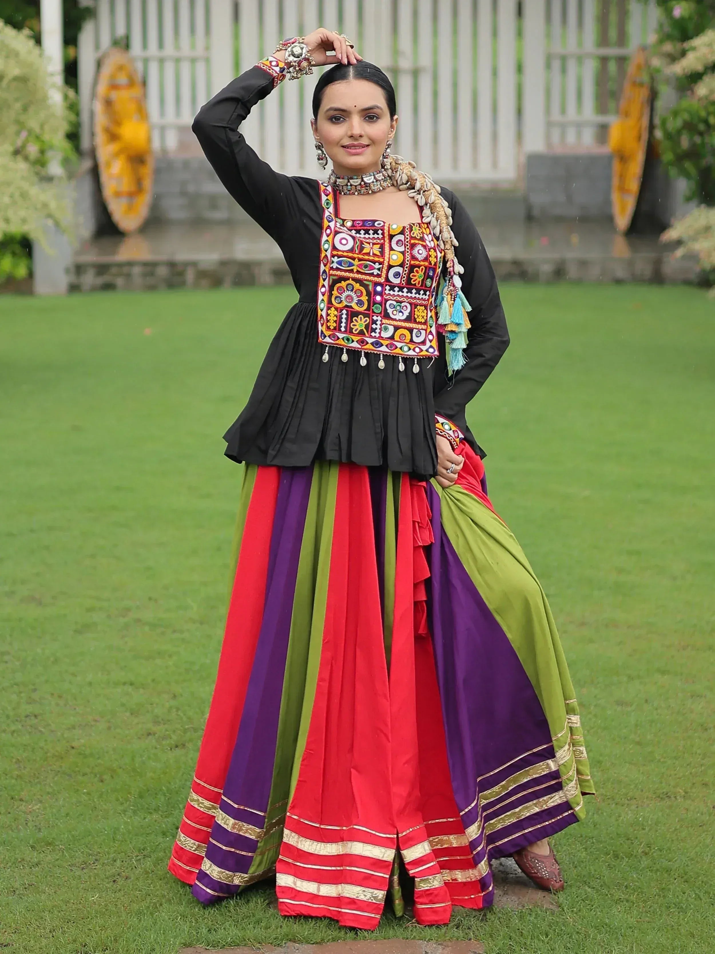 Woman in vibrant Indian ethnic wear: black embroidered top with colorful striped skirt, perfect for festive occasions.
