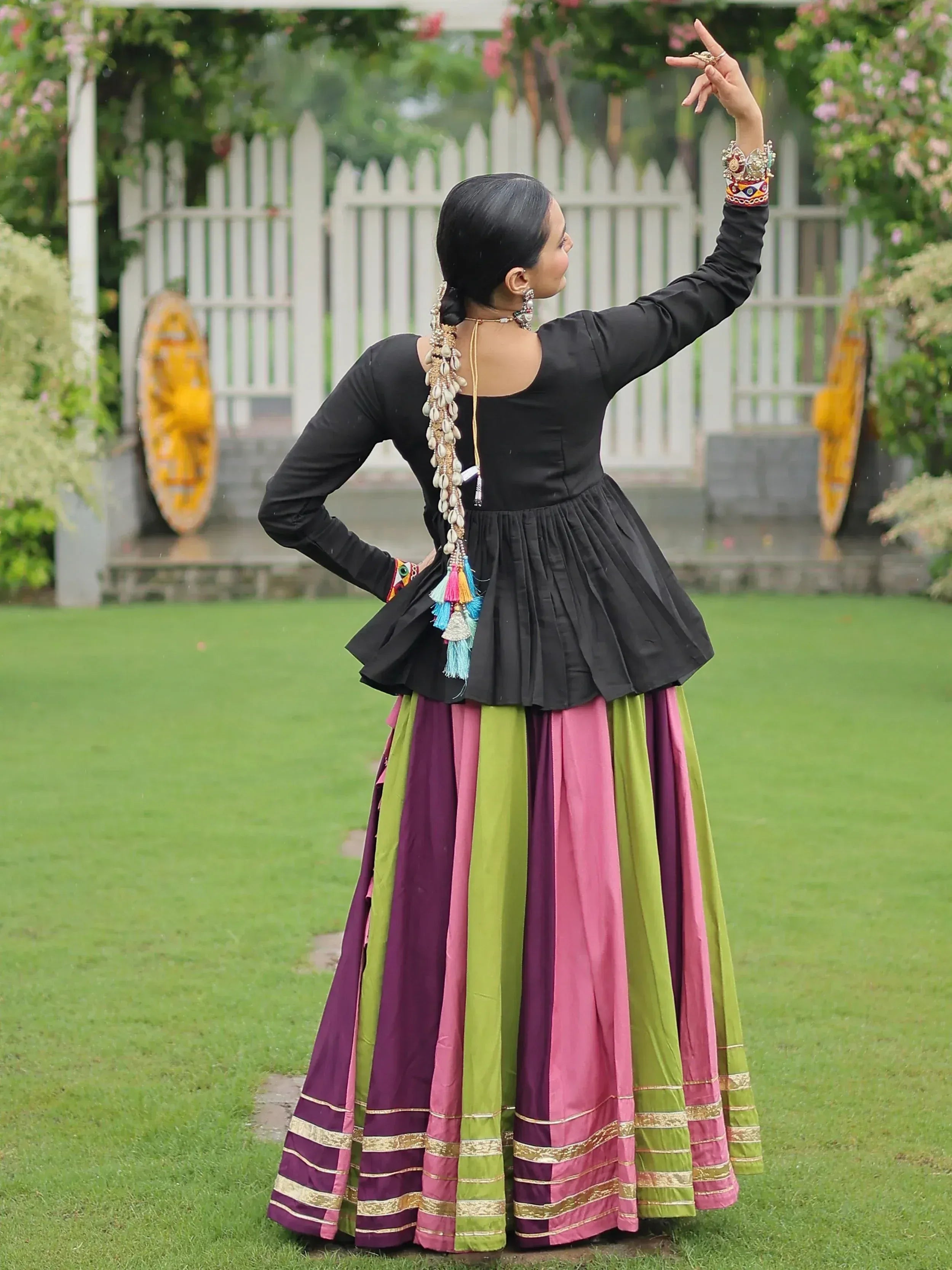 Woman in black peplum top and colorful striped ethnic skirt, posing outdoors with traditional jewelry.