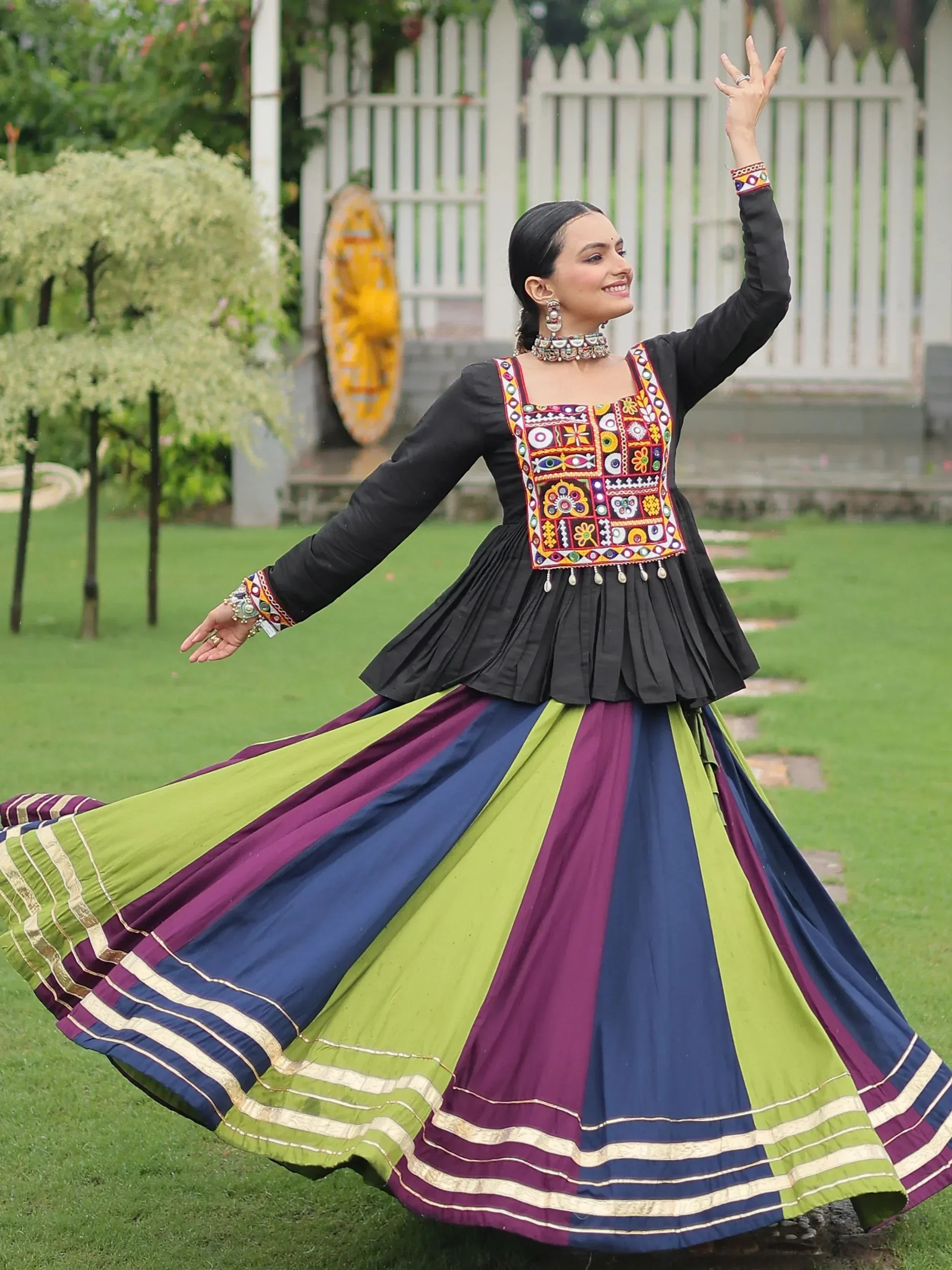 Woman in black embroidered top and colorful striped lehenga, dancing outdoors
