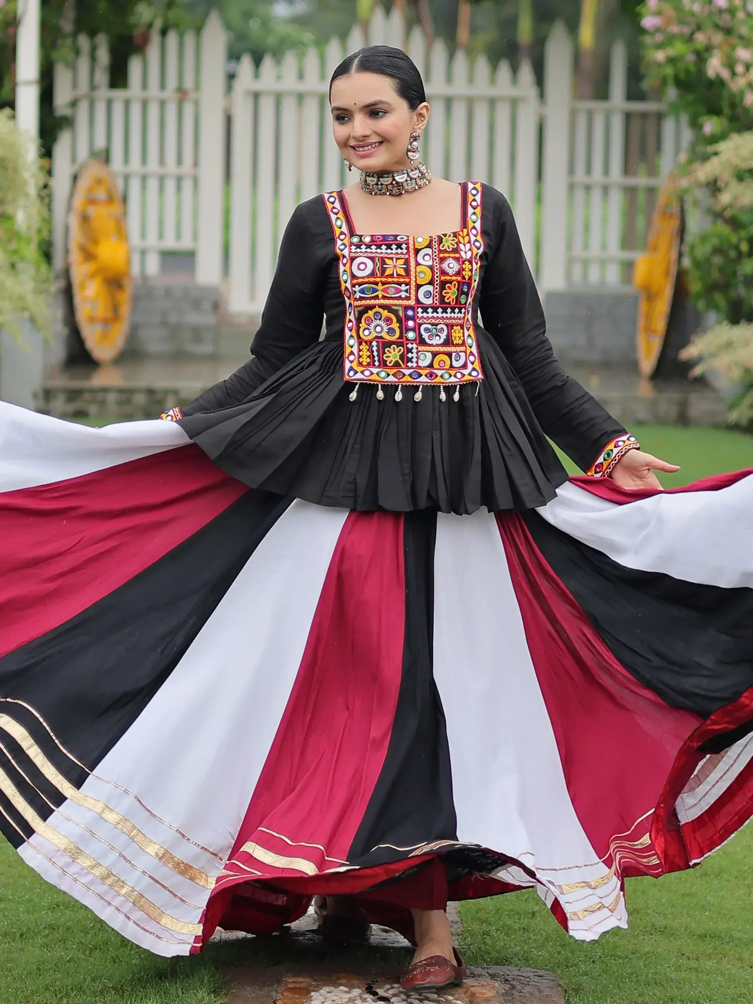 Woman in black embroidered top with colorful mirror work and flowing red, white, black skirt, Indian ethnic wear