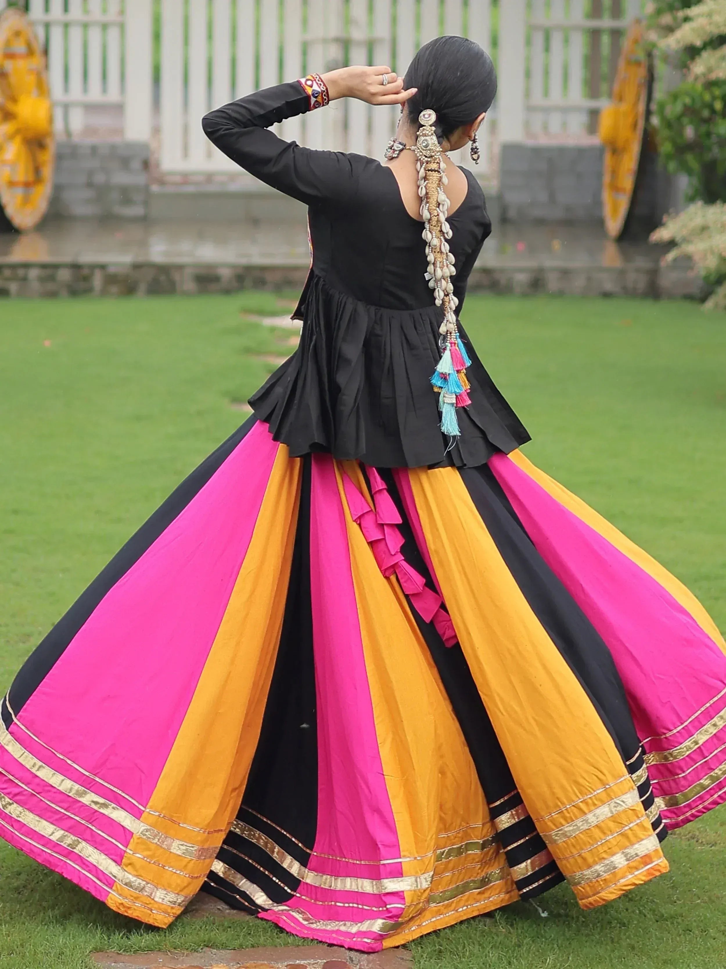 Woman in black top and vibrant pink, yellow, black striped lehenga with tassels, showcasing ethnic Indian wear