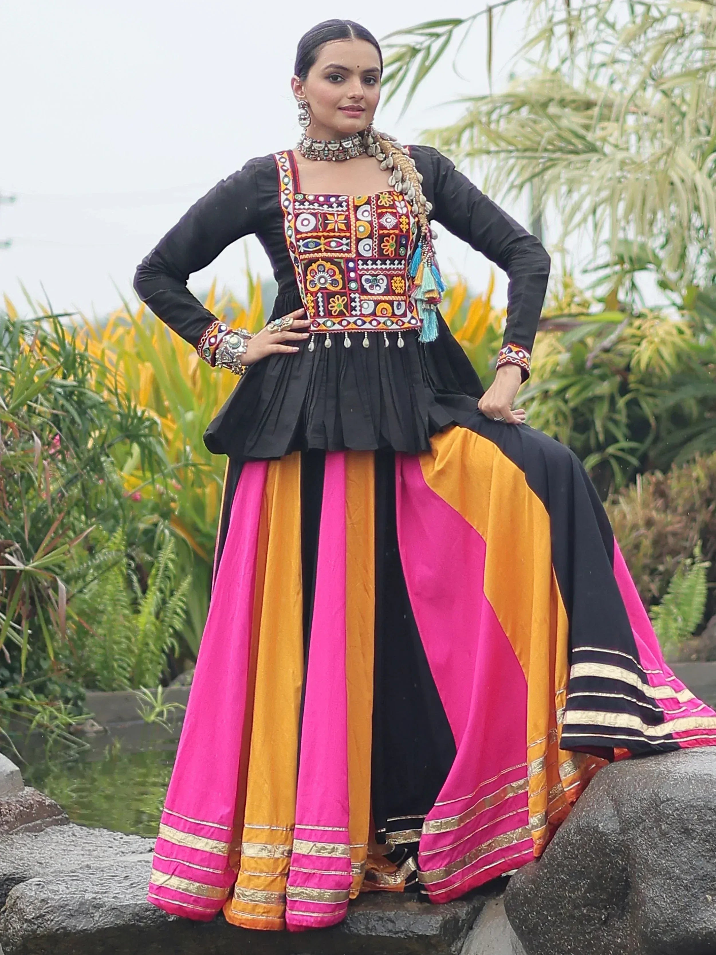 Woman in black embroidered top with vibrant pink and orange skirt, traditional Indian ethnic wear