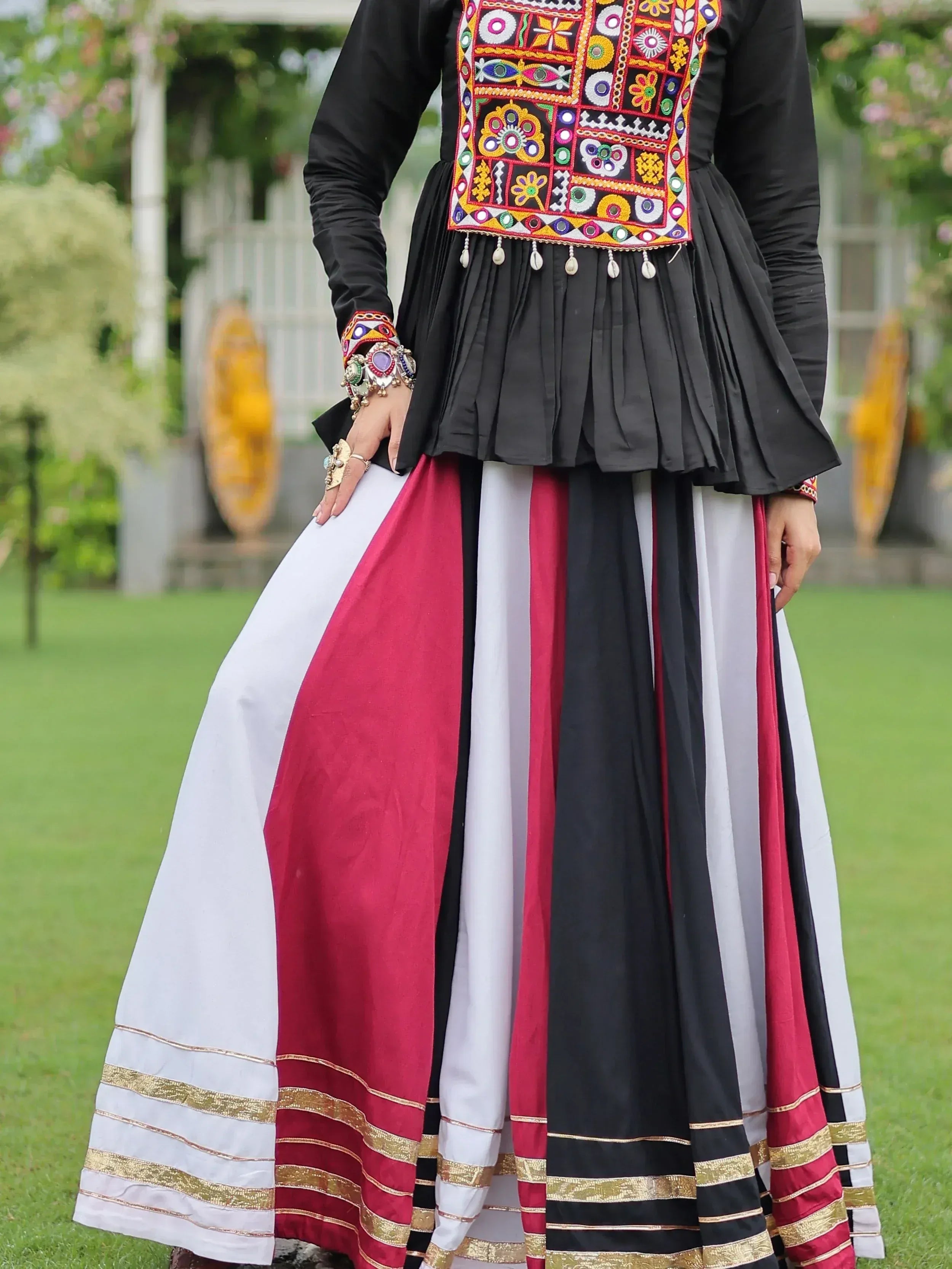 Black embroidered top with colorful mirror work, paired with striped white, red, and black skirt, ethnic wear