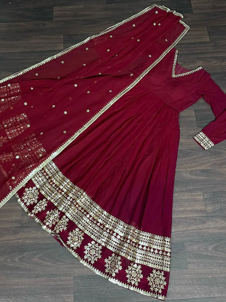 Maroon Indian ethnic gown with gold embroidery and matching dupatta on wooden floor