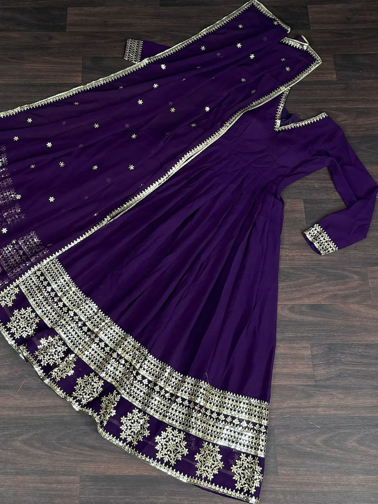 Purple embroidered ethnic gown with gold detailing and matching dupatta on wooden floor