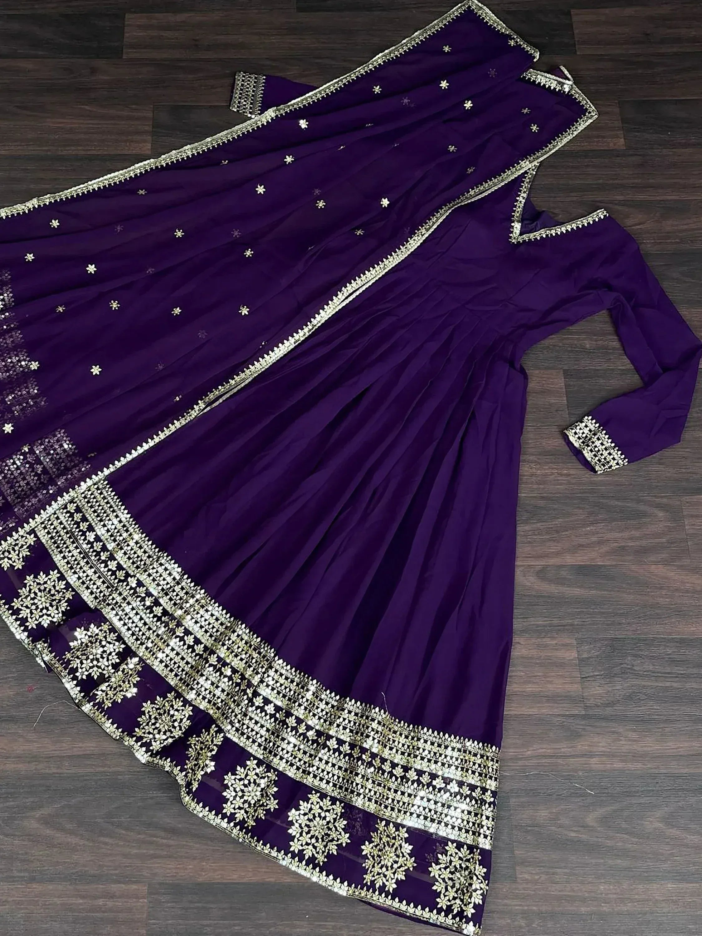 Purple embroidered ethnic gown with gold detailing and matching dupatta on wooden floor