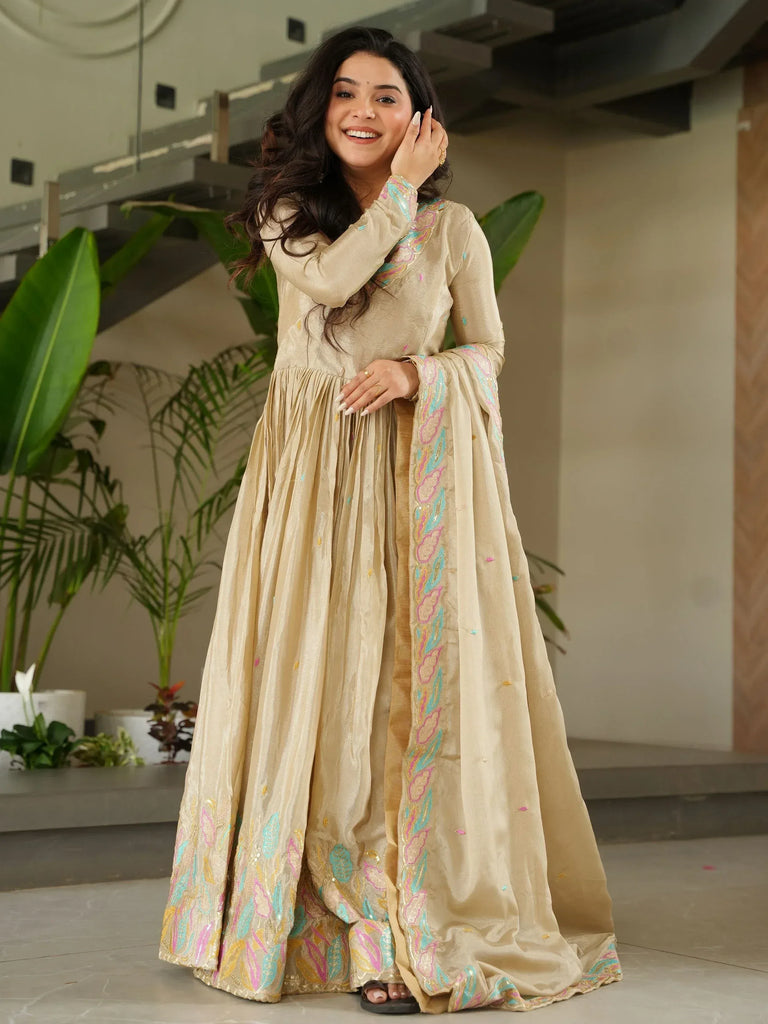 Beige embroidered ethnic gown with colorful floral patterns, perfect for Indian festive occasions.