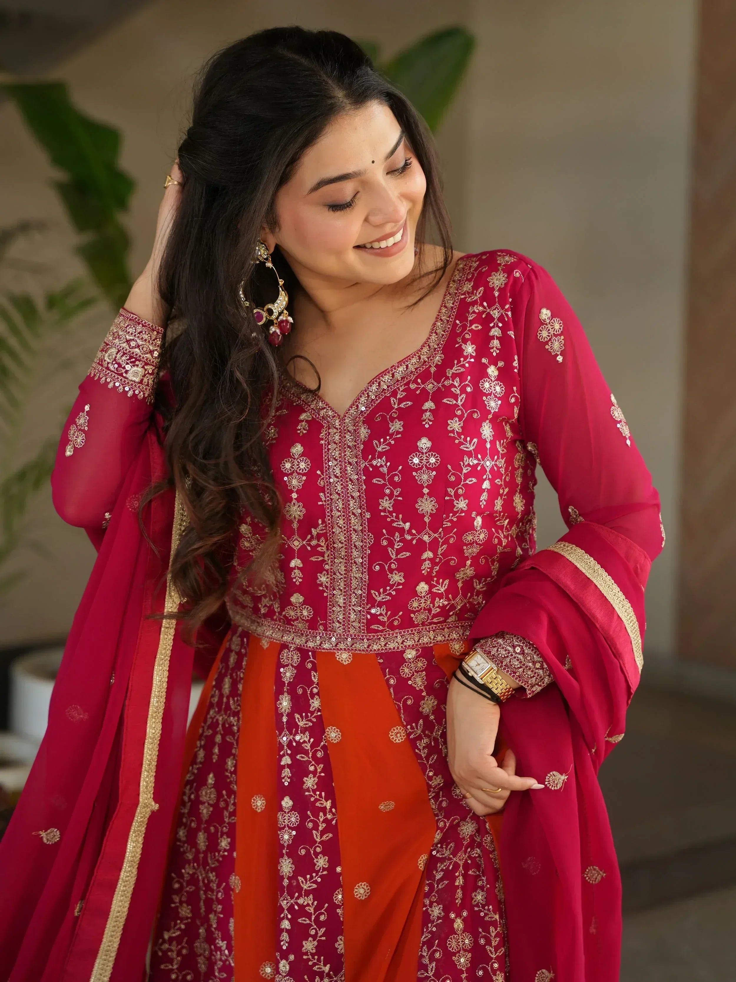 Woman in red and orange embroidered Indian ethnic wear with gold detailing, perfect for festive occasions.
