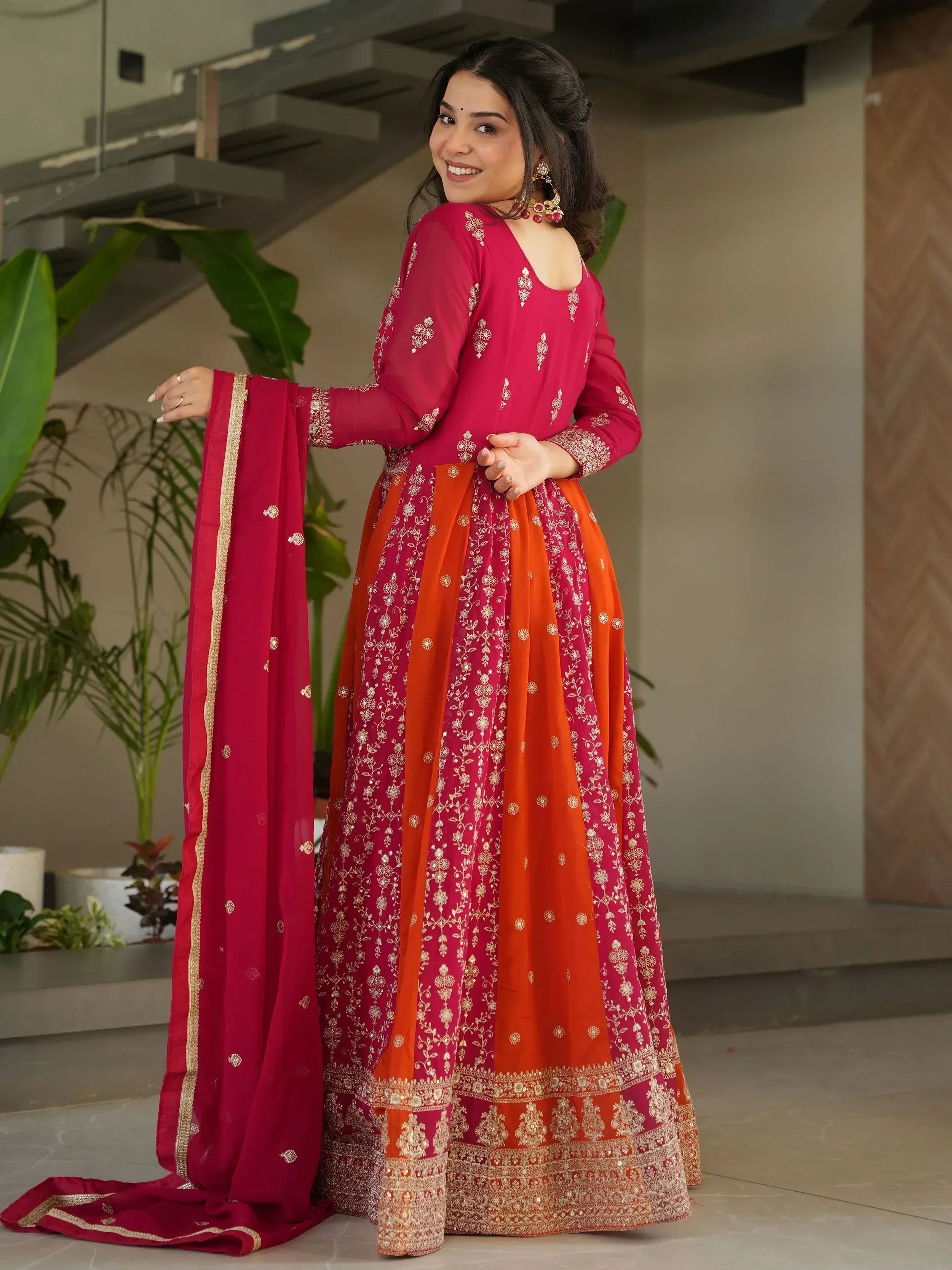 Woman in vibrant red and orange embroidered Indian anarkali suit with gold detailing, perfect for festive occasions.