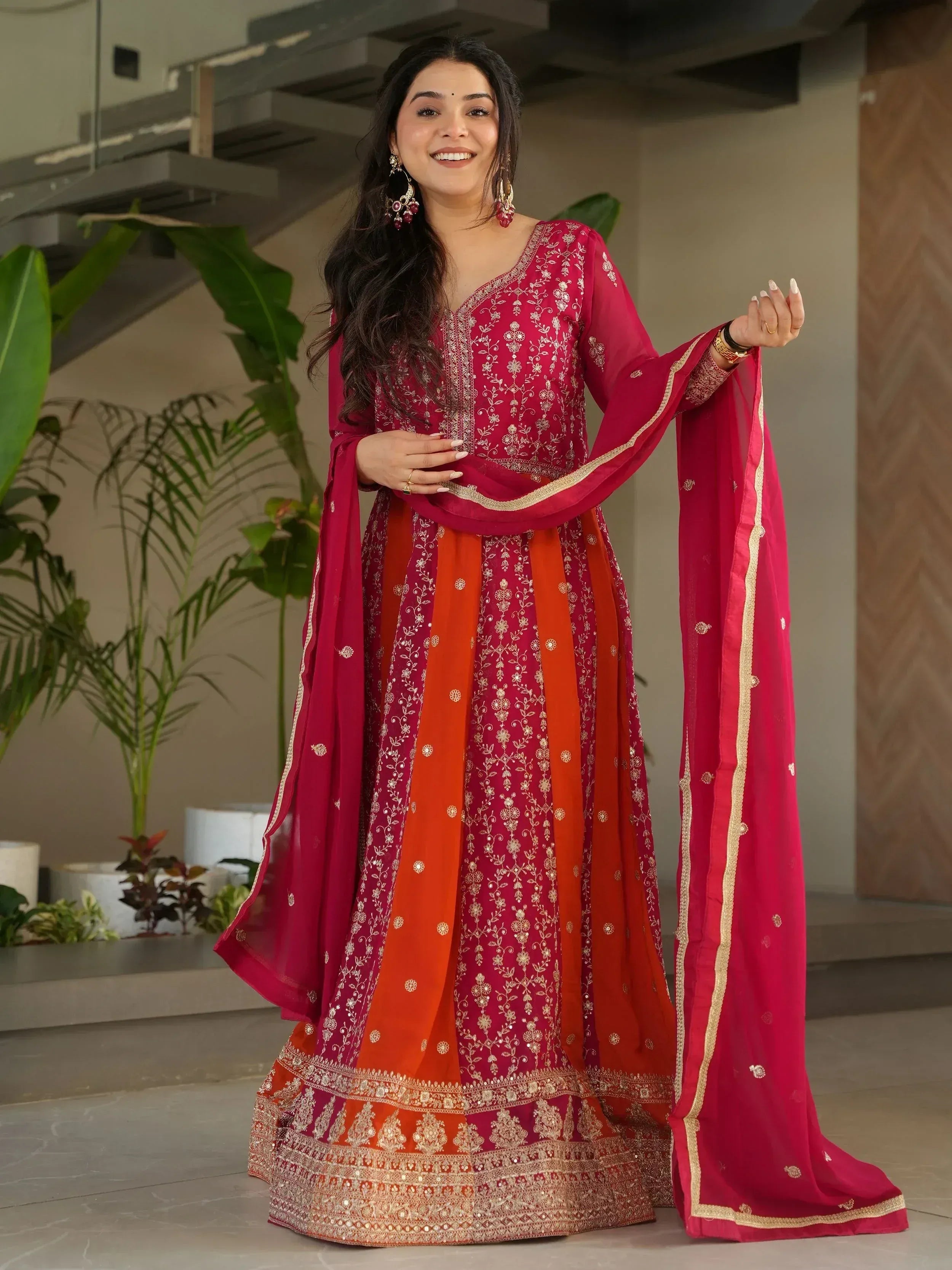 Woman in red and orange embroidered Indian ethnic wear with gold detailing, perfect for festive occasions.