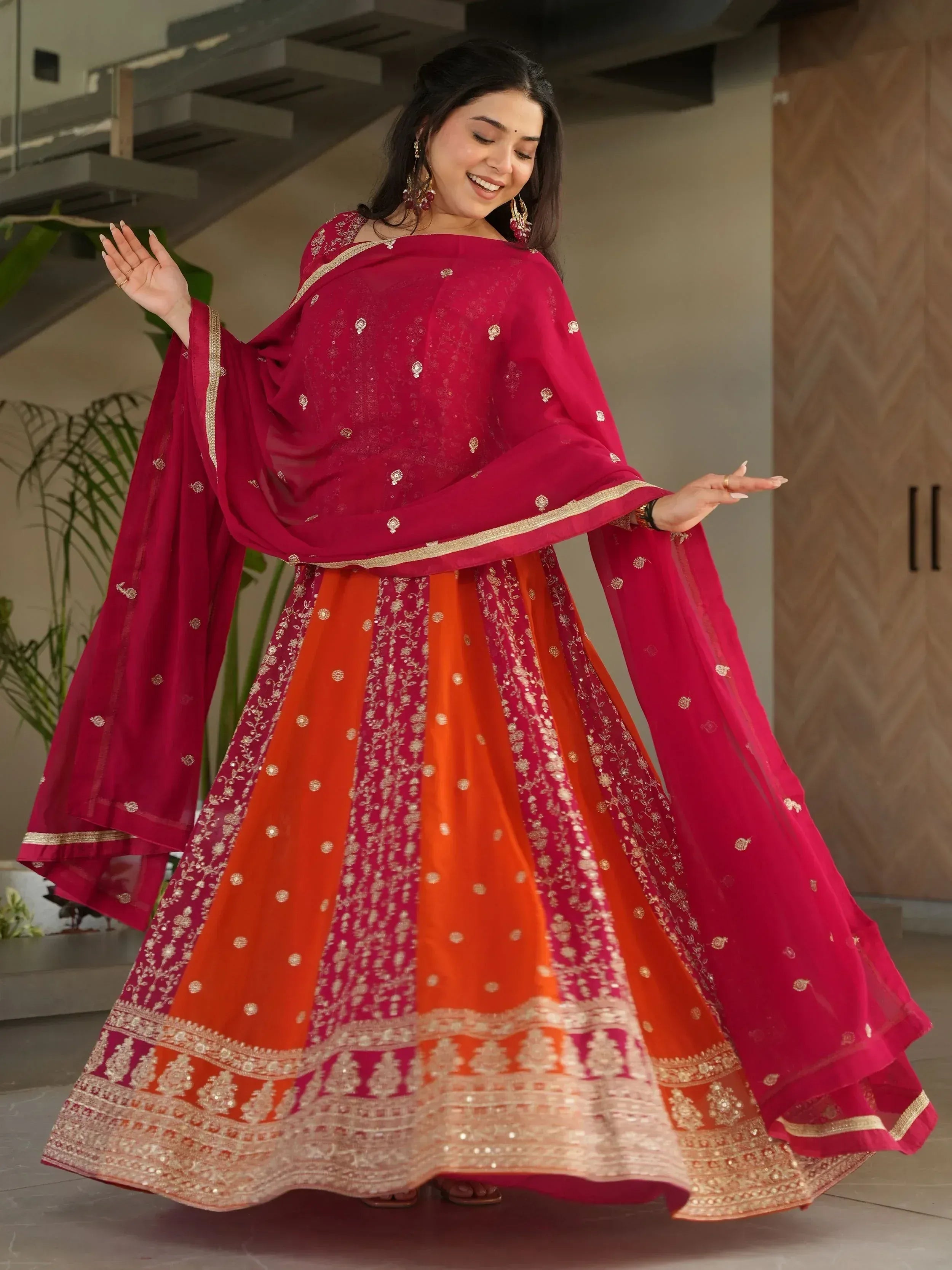 Woman in vibrant red and orange embroidered lehenga choli with gold detailing, perfect for Indian ethnic wear occasions.