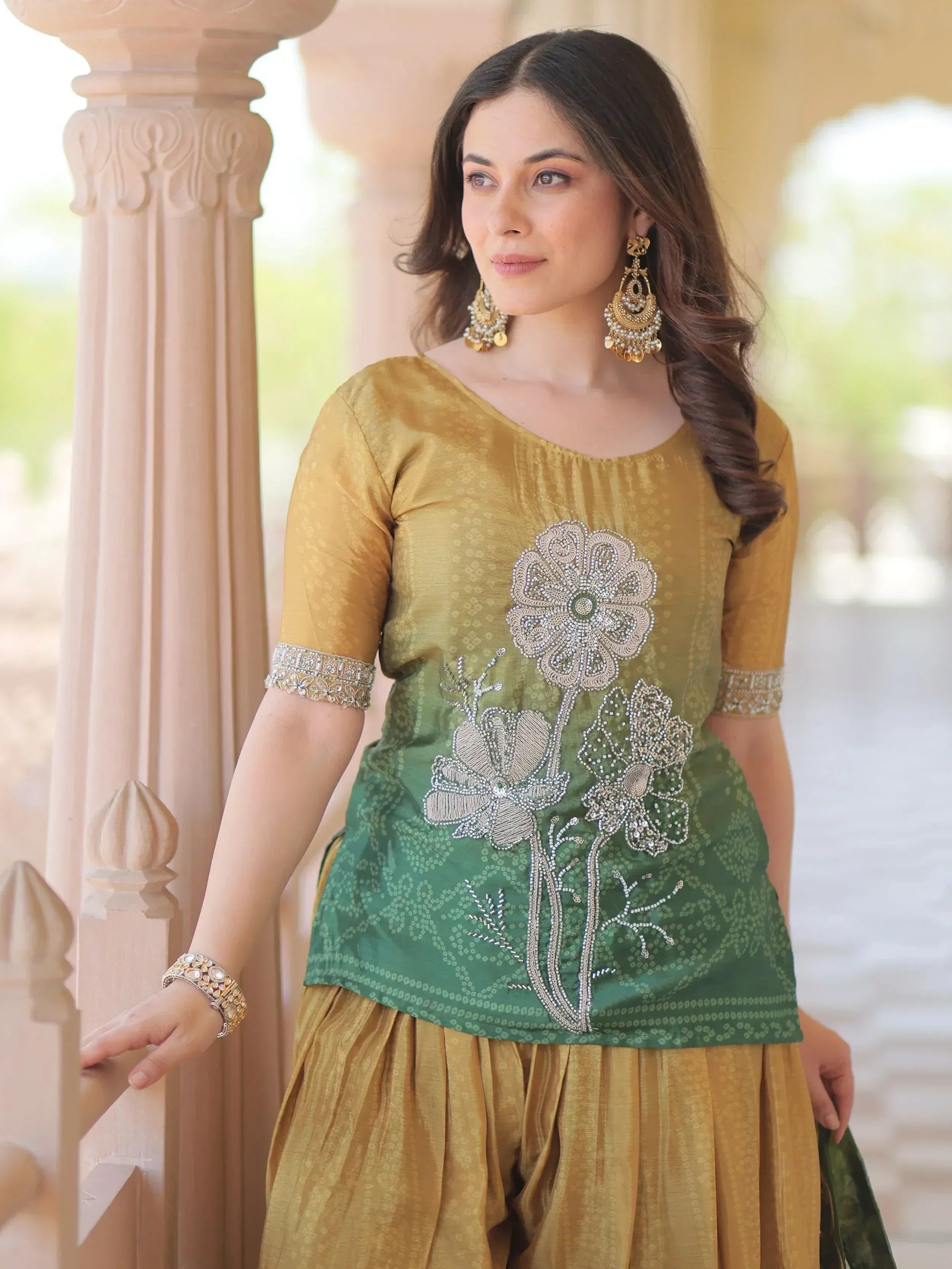 Woman in mustard and green ethnic salwar kameez with floral embroidery and gold jewelry